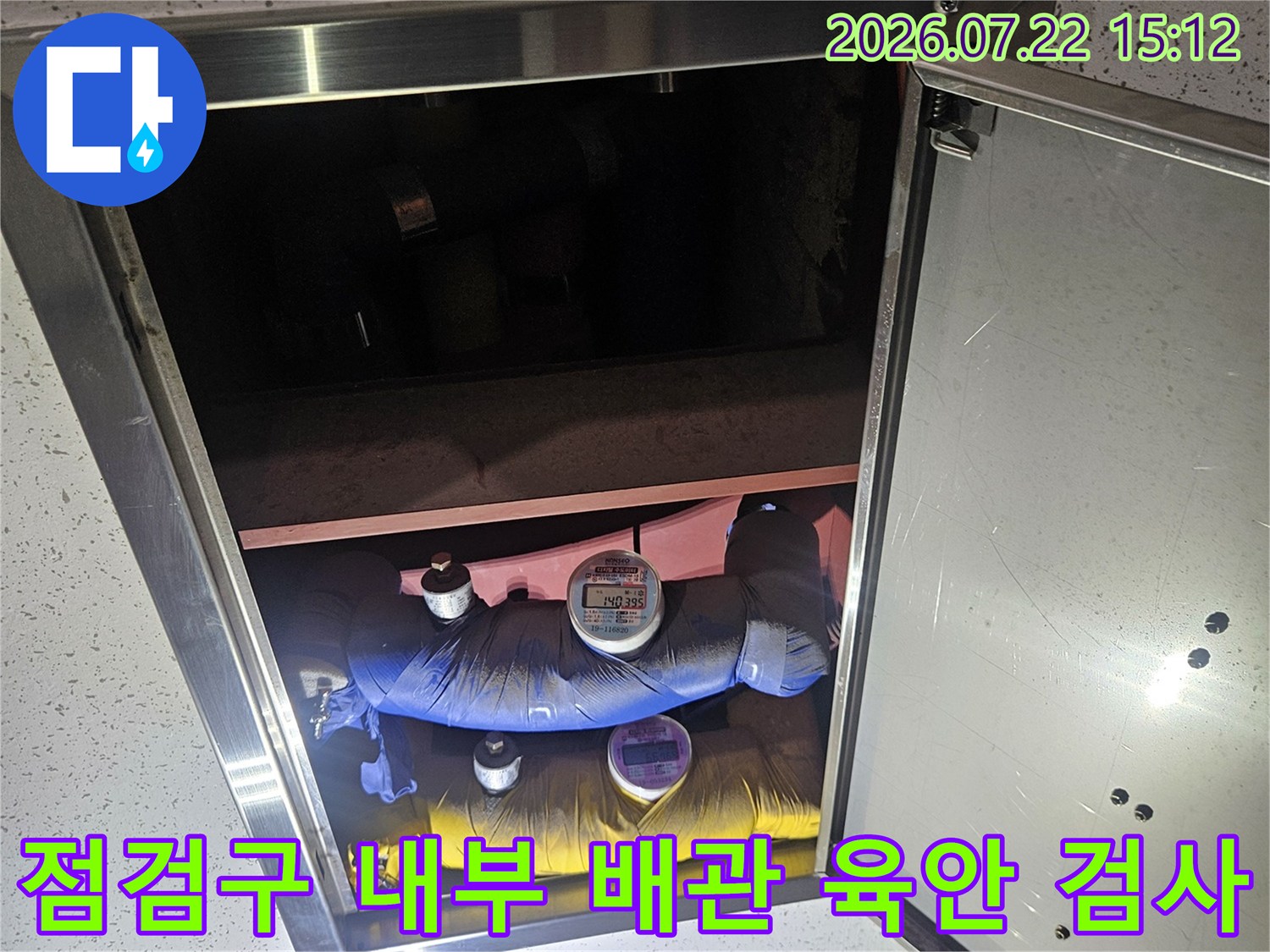화장실 천장 점검구를 열어 보온재로 마감된 파란색과 노란색 배관을 살피는 사진
