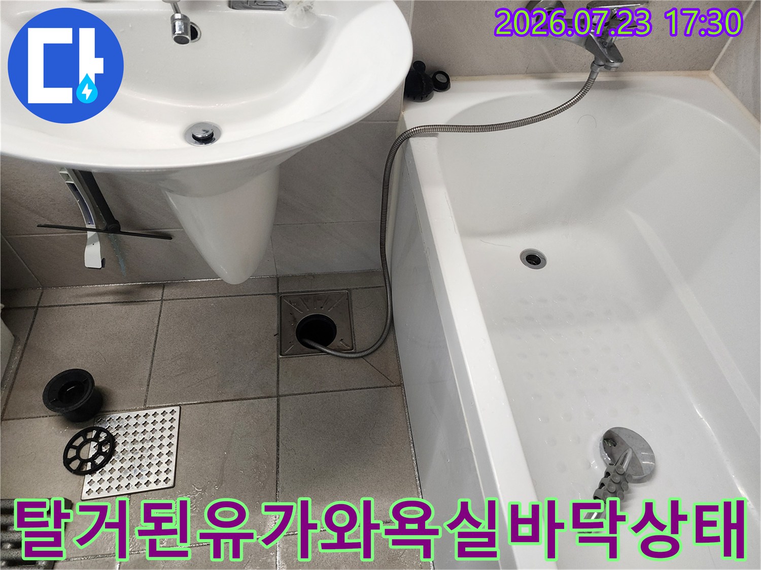 화장실 바닥 배수구 유가가 열려 있고 옆에 세면대와 욕조가 배치된 사진