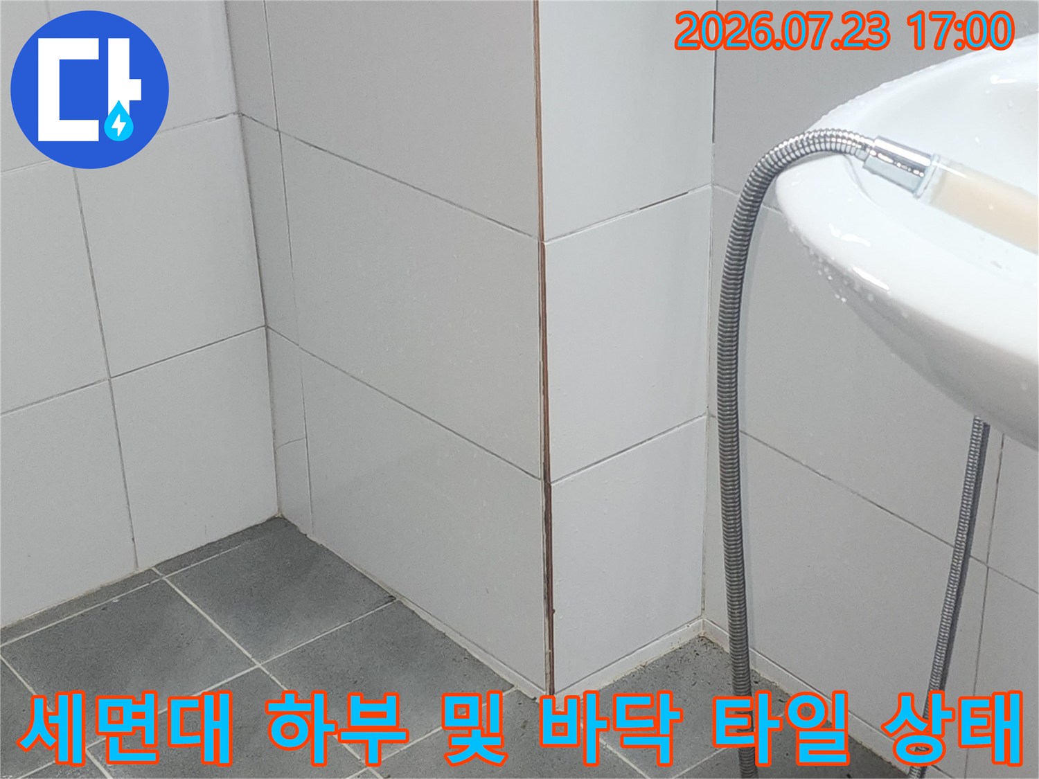흰색 세면대 아래로 샤워 호스가 늘어져 있으며 바닥과 벽면에 흰색 타일이 시공된 모습