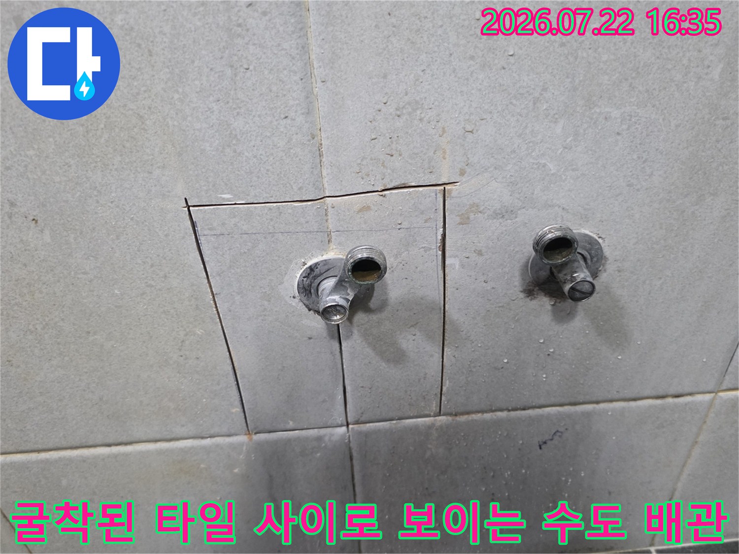 타일 벽면의 일부를 사각형으로 파내어 내부의 금속제 수도 연결 관이 드러나 있는 사진