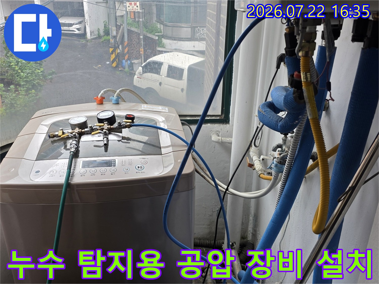 파란색 호스와 압력 게이지가 연결된 누수 탐지 장비가 세탁기 위에 놓여 있는 모습