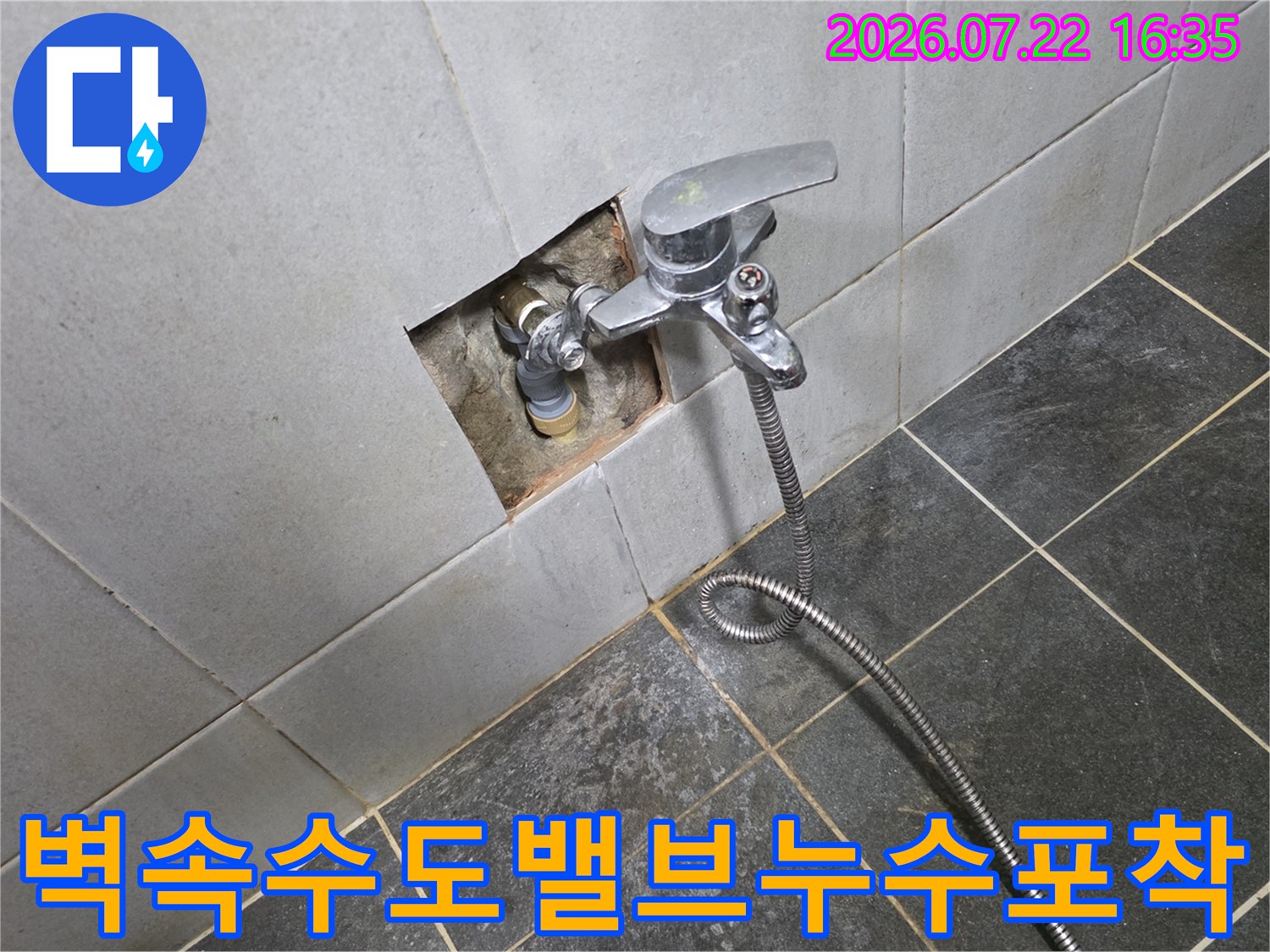 흰색 타일 벽면의 일부가 파여 있으며 그 안에 설치된 금속 수도 밸브가 노출된 모습