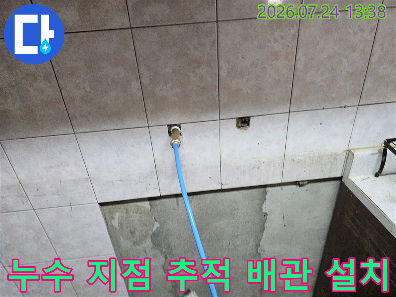 회색 타일 벽면에 파란색 플라스틱 배관이 돌출되어 연결된 사진