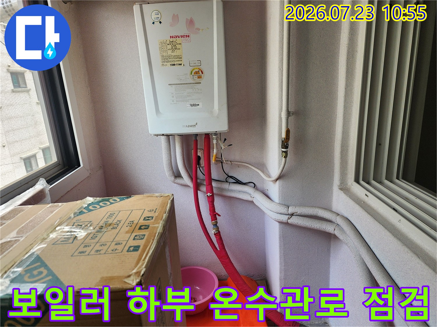 흰색 가스보일러 아래로 설치된 빨간색 온수 배관과 벽면의 연결 부위 상세 사진