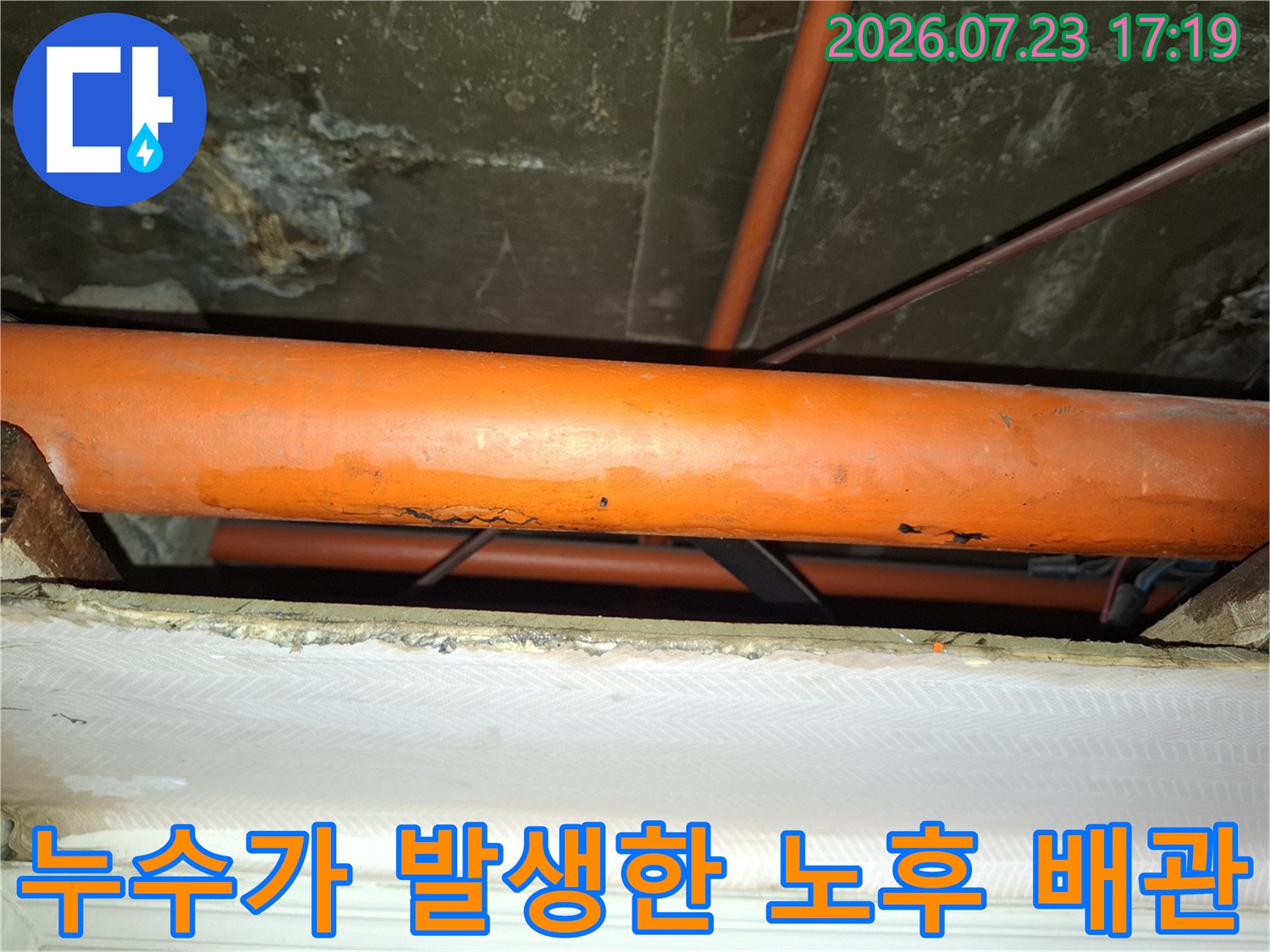 천장 슬라브 아래 위치한 부식된 오렌지색 배관과 주변의 습기 흔적-사진