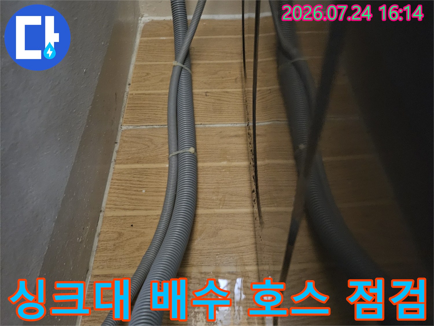 싱크대 하부의 여러 갈래로 뻗은 회색 배수 호스와 벽면 연결 부위