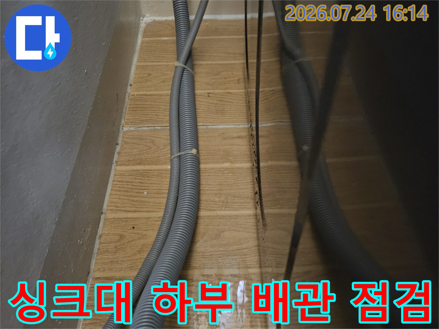 회색 주름관 형태의 배수 호스가 벽면 배출구를 향해 연결된 모습
