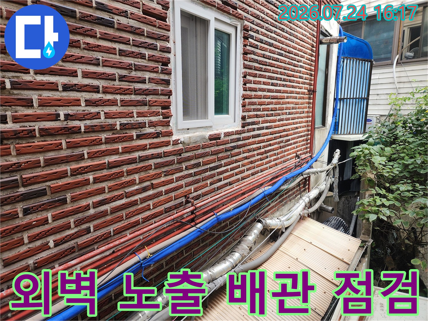 붉은 벽돌 외벽에 노출된 파란색과 은색 단열재 배관 상태를 점검하는 모습