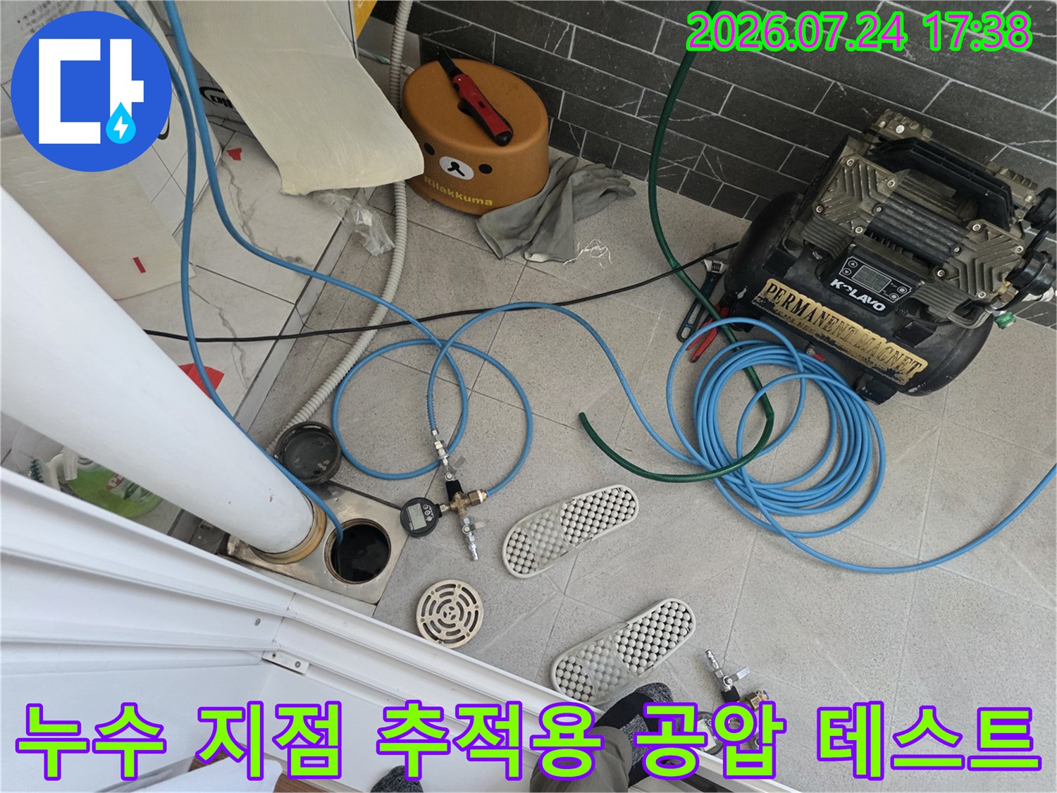 파란색 호스와 콤프레샤 장비를 연결하여 화장실 배관 시스템의 기밀 상태를 점검하는 모습
