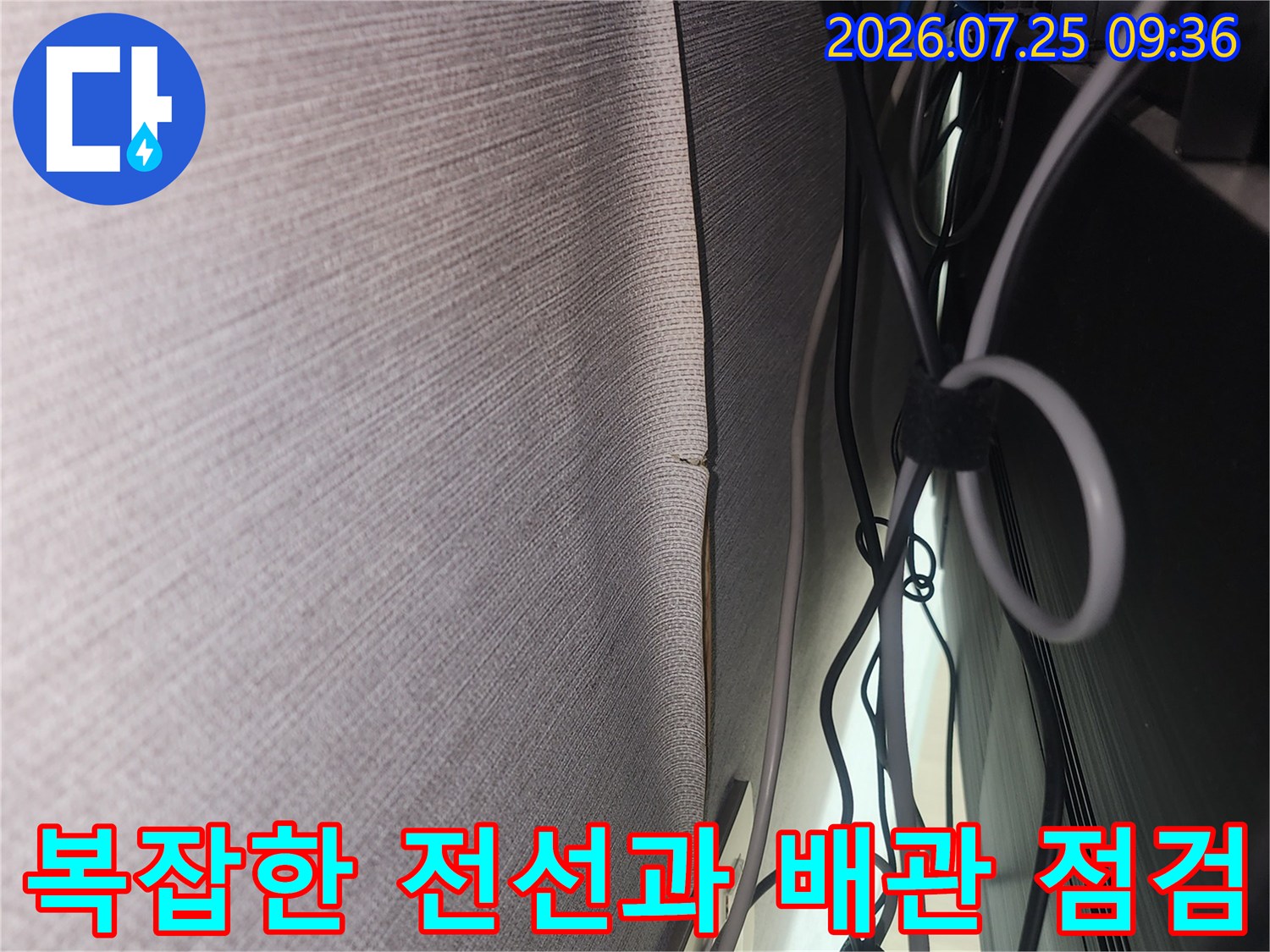 어두운 벽면 뒤로 복잡하게 얽힌 전기선과 수조용/상수도용 배관을 확인하는 모습