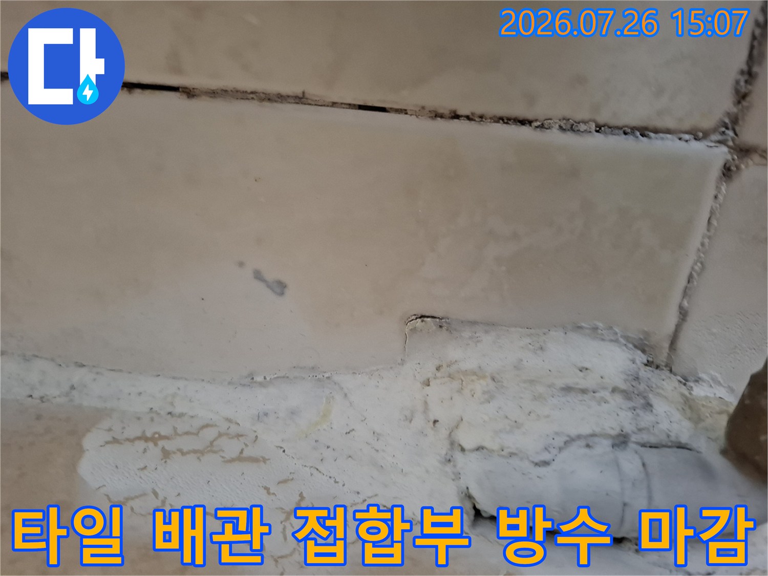 베이지색 욕실 타일 하단 배관 연결 부위에 흰색 보강재가 채워진 장면