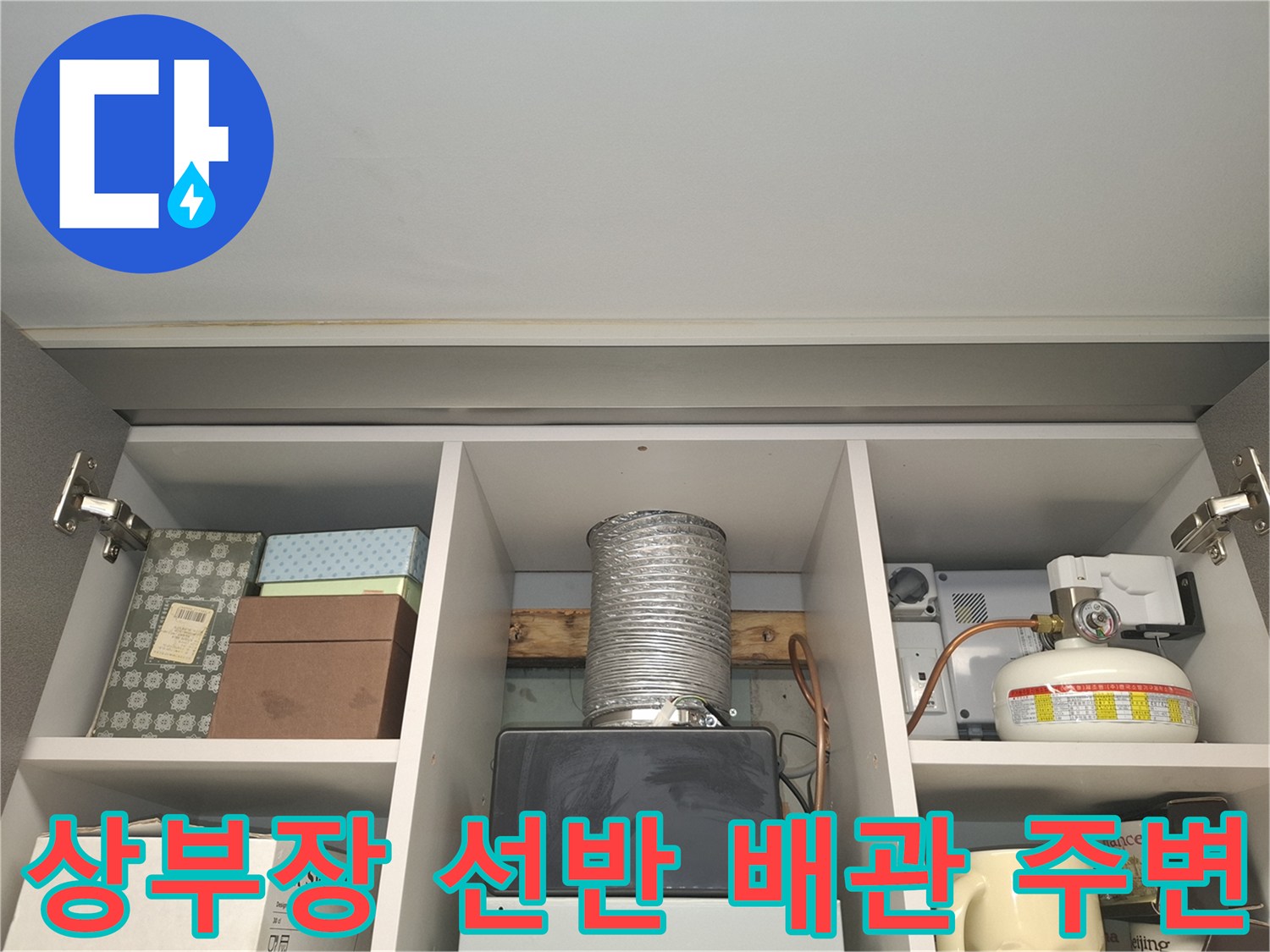 싱크대 상부장 선반에 놓인 은색 원통형 자재와 박스류