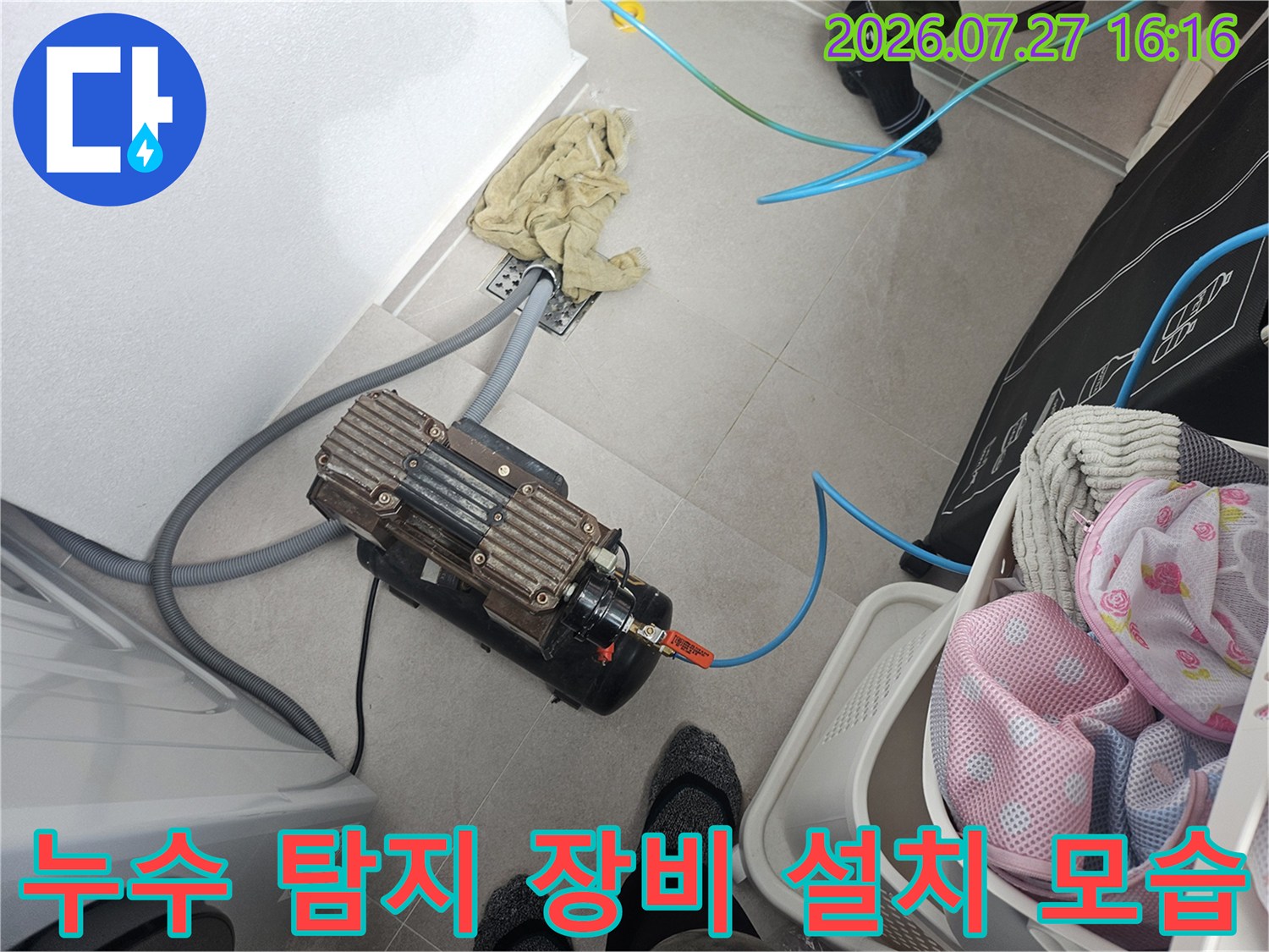 바닥에 놓인 전문 누수 탐지 압력 장비와 연결된 파란색 호스-배관 점검 중