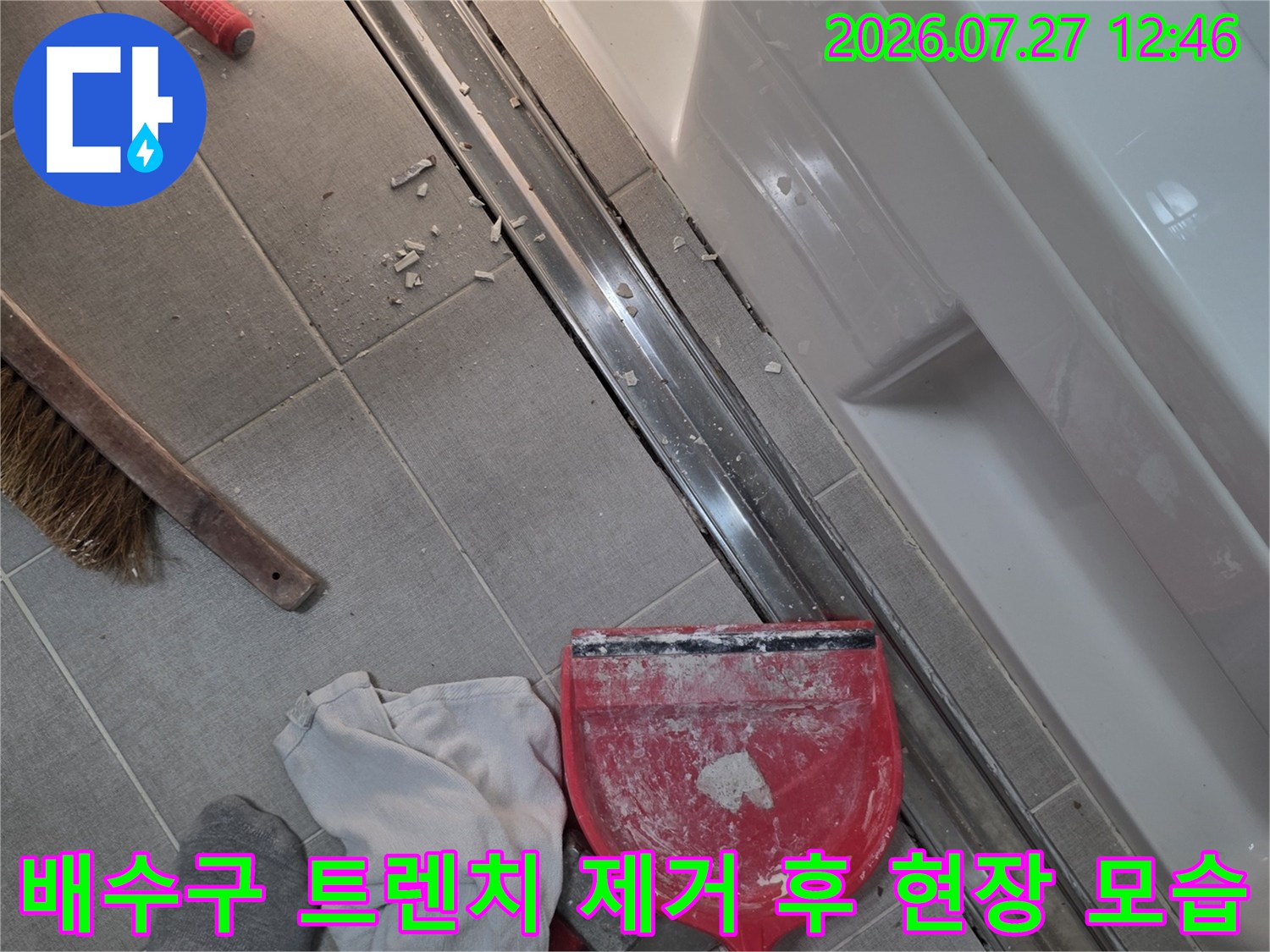 금속 배수 트랜치가 제거된 틈새와 그 옆에 놓인 작업용 청소 도구들-걸레와 빗자루