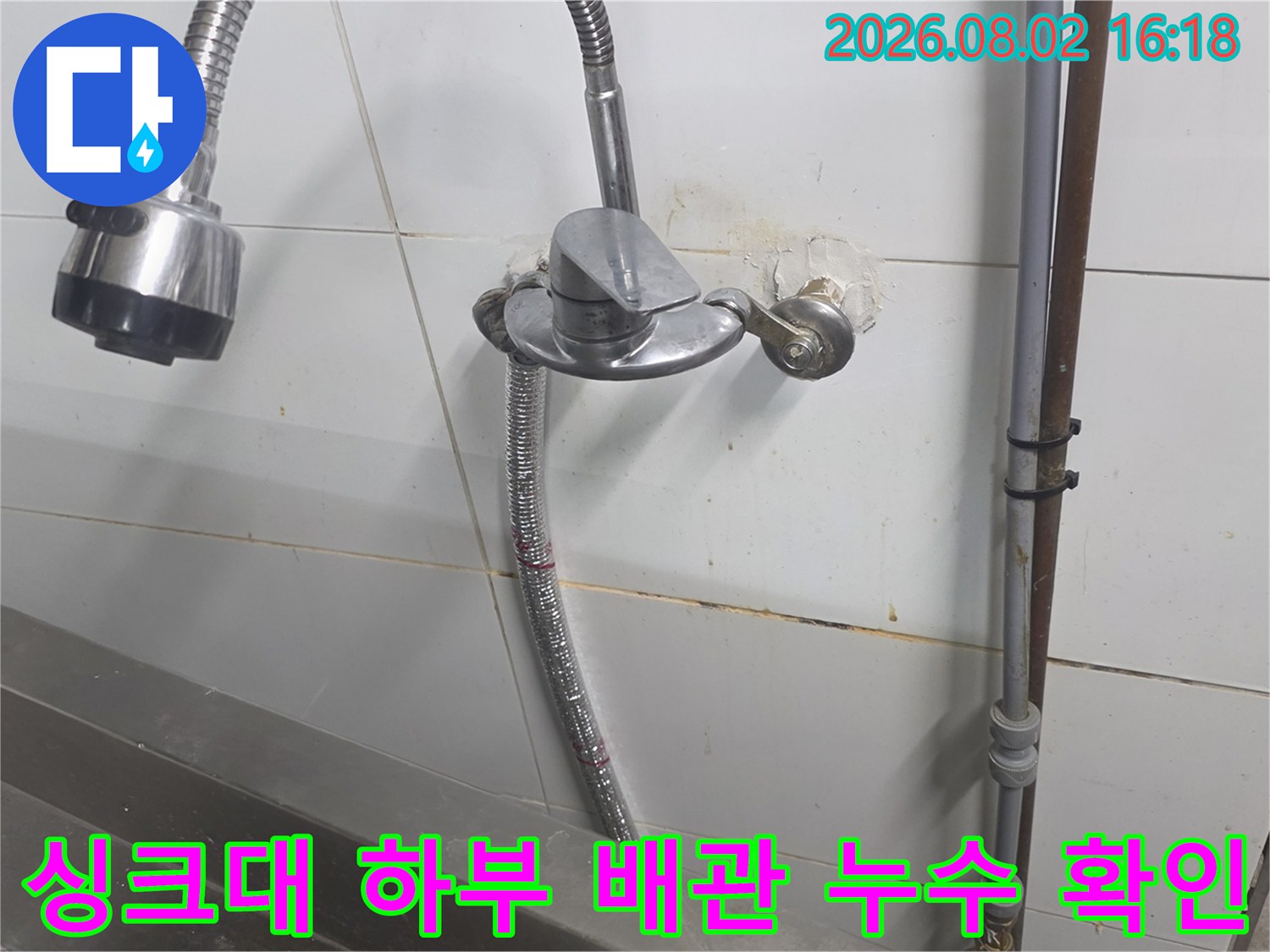 싱크대 아래쪽 벽면 타일과 연결된 급수 배관의 상태 점검 장면