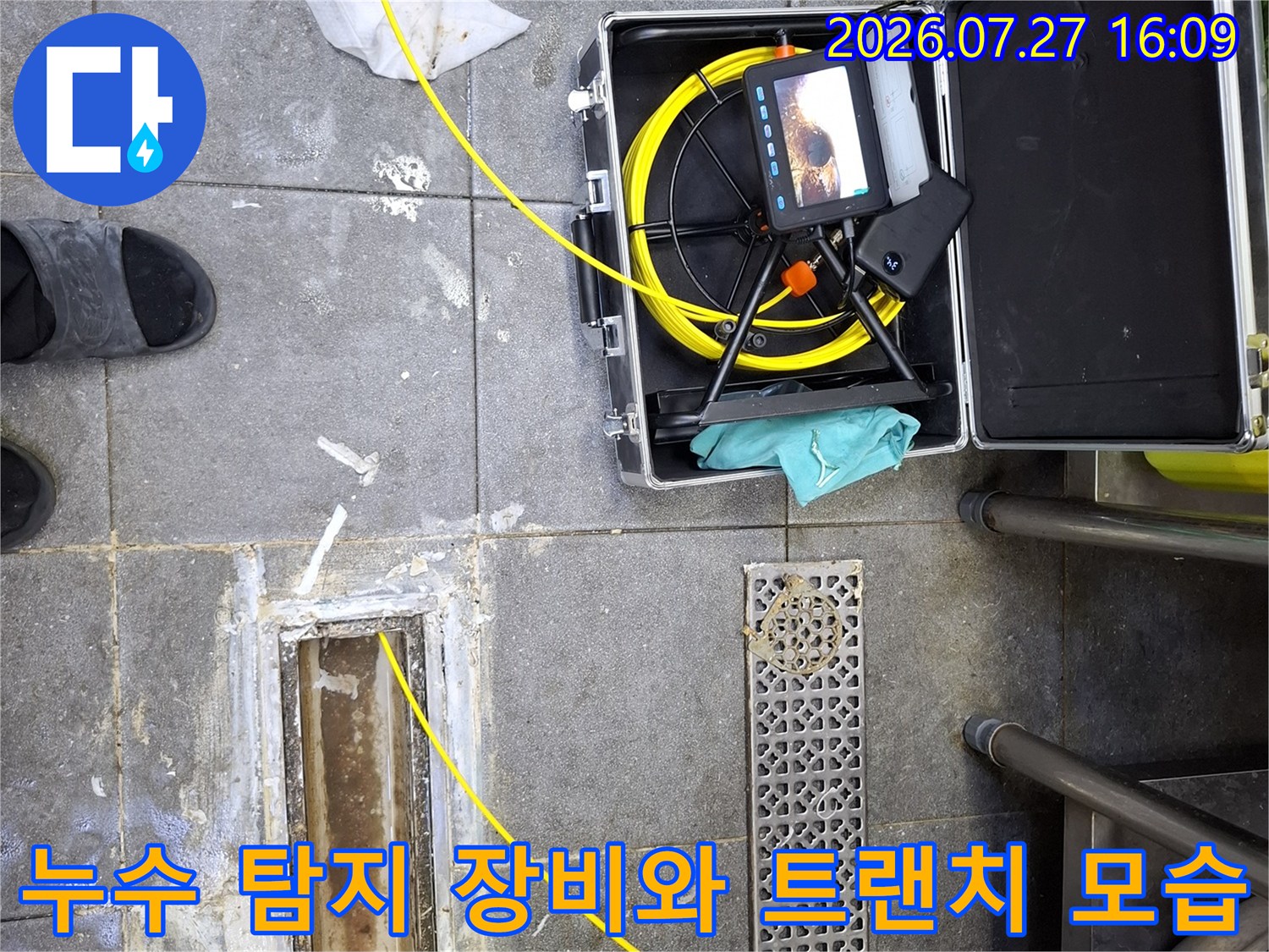 모니터가 달린 내시경 장비 케이스가 바닥에 놓여 있고 노란색 선이 배수구 안쪽으로 연결된 사진