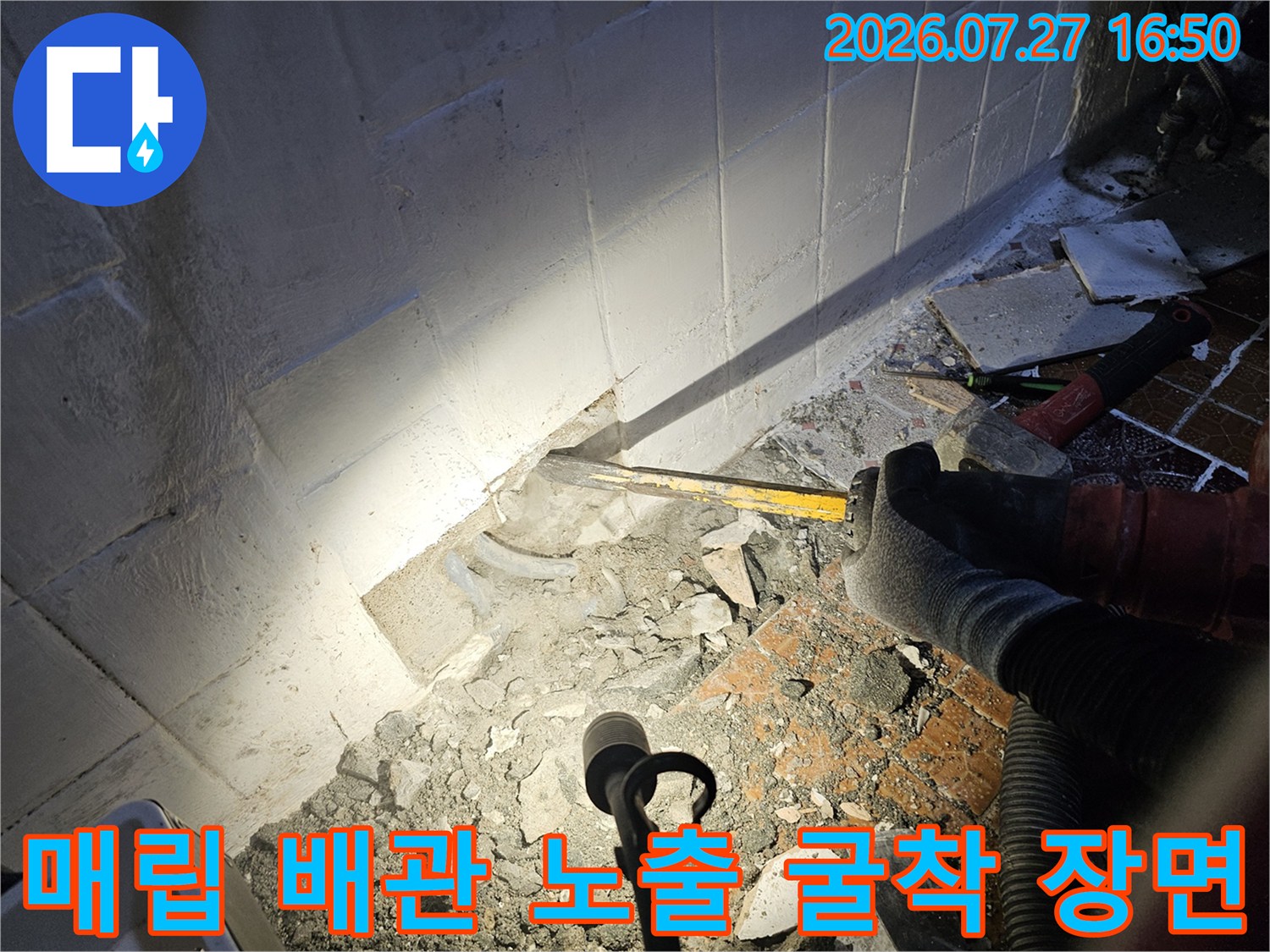 노란색-공구를-잡은-작업자의-손과-바닥에-드러난-하얀색-배관-그리고-주변의-콘크리트-파편들