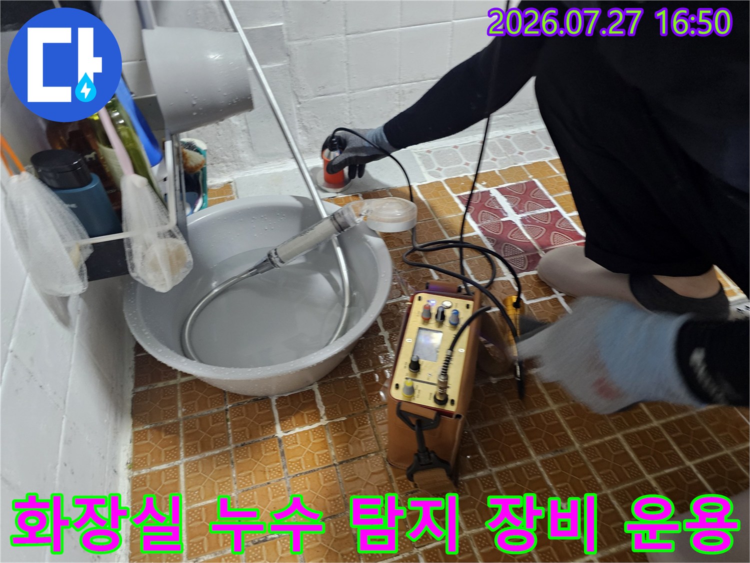 욕실 바닥에 놓인 노란색 정밀 누수 탐지기와 배관 연결 호스-작업자가 장비를 조절하는 모습
