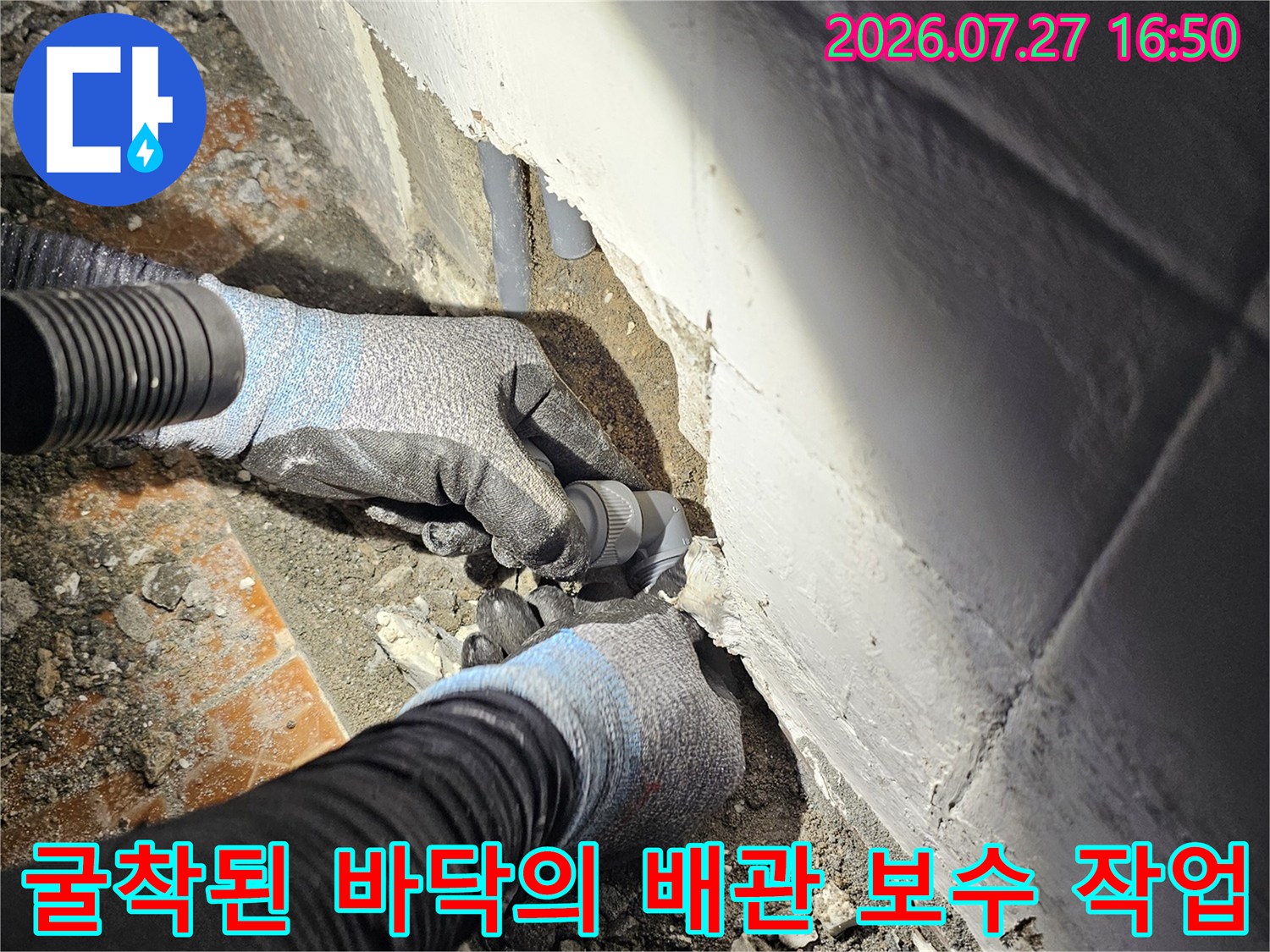 작업자가 장갑을 착용하고 화장실 바닥 타일을 걷어낸 후 드러난 회색 배관 부속을 만지고 있는 모습