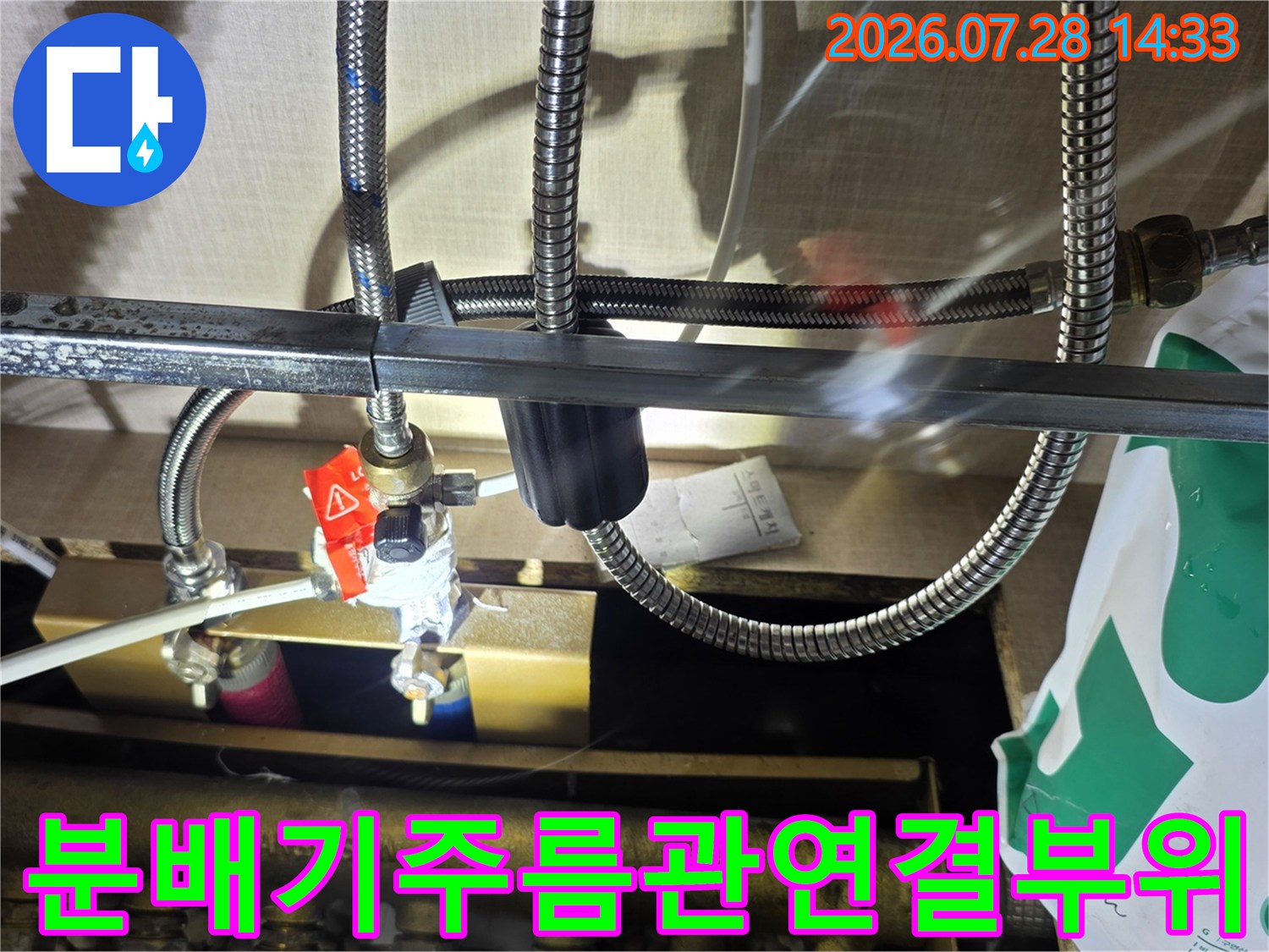 붉은색 핸들이 있는 분배기와 연결된 배관의 누수 부위를 촬영한 사진