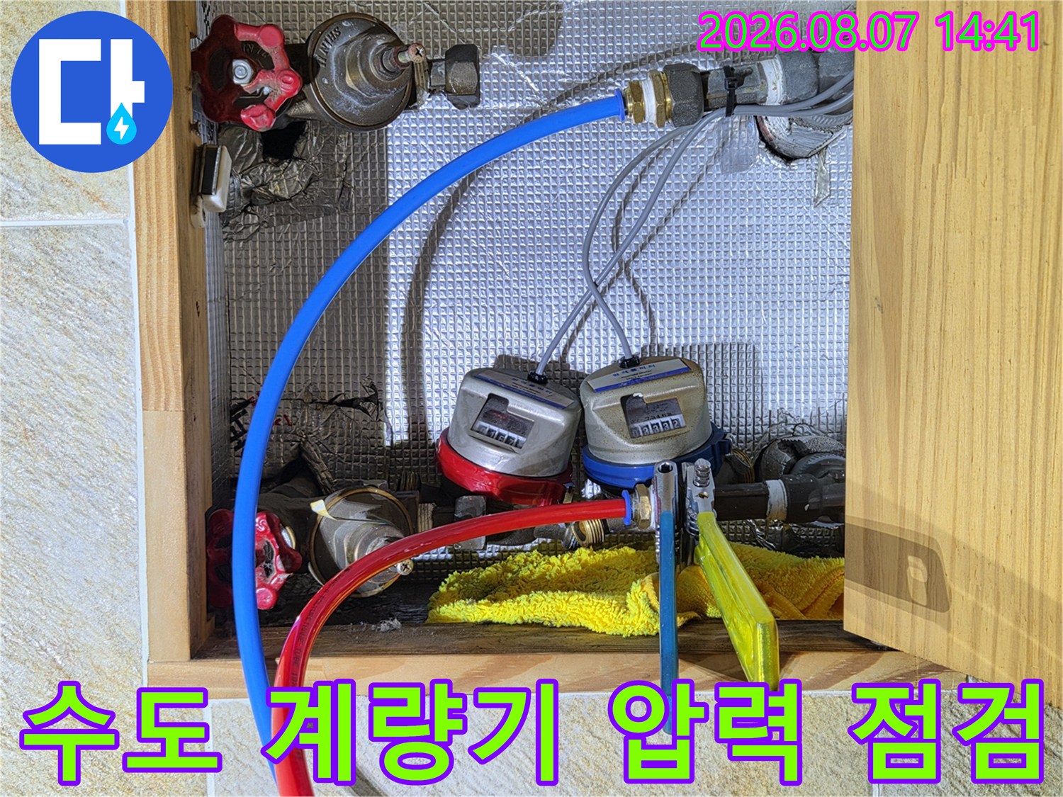 수도 계량기에 파란색과 빨간색 호스를 연결하여 배관의 압력을 테스트하는 모습입니다.
