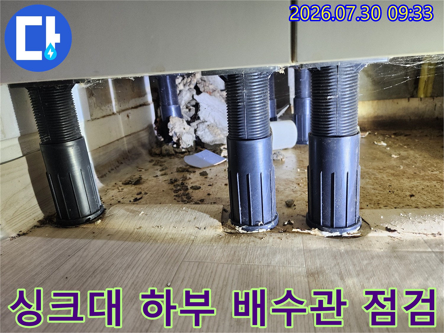 싱크대 아래 수직으로 세워진 검은색 배수용 파이프와 바닥 연결 부위 상태를 확인하는 모습