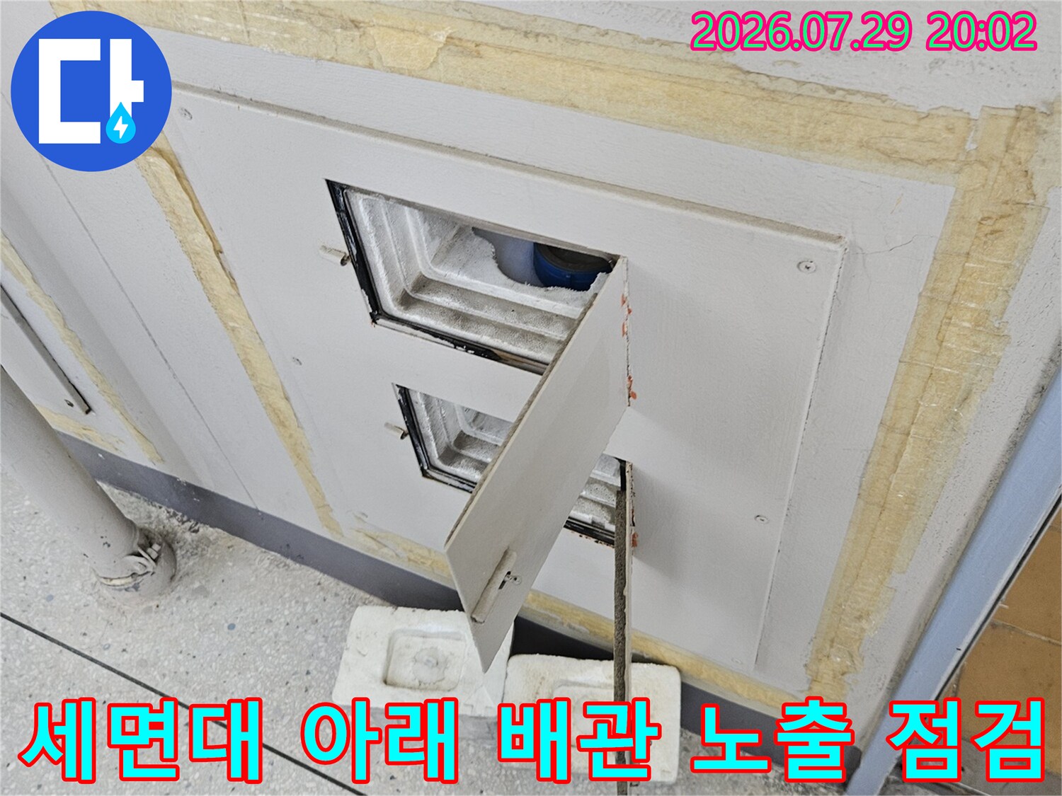 노출된 세면대 하부 공간에서 수도 배관의 연결 상태를 면밀히 검사하는 현장