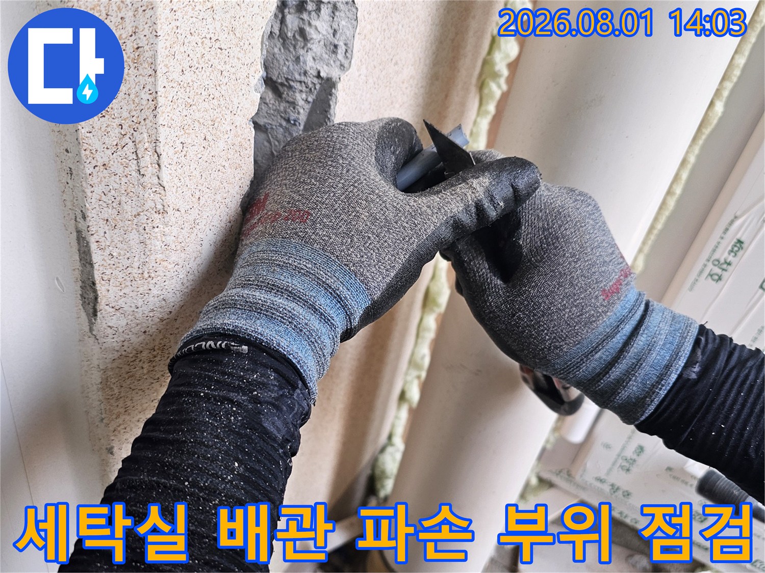 작업자가 장갑을 끼고 세탁실 타일 벽면의 노출된 배관을 점검하는 모습