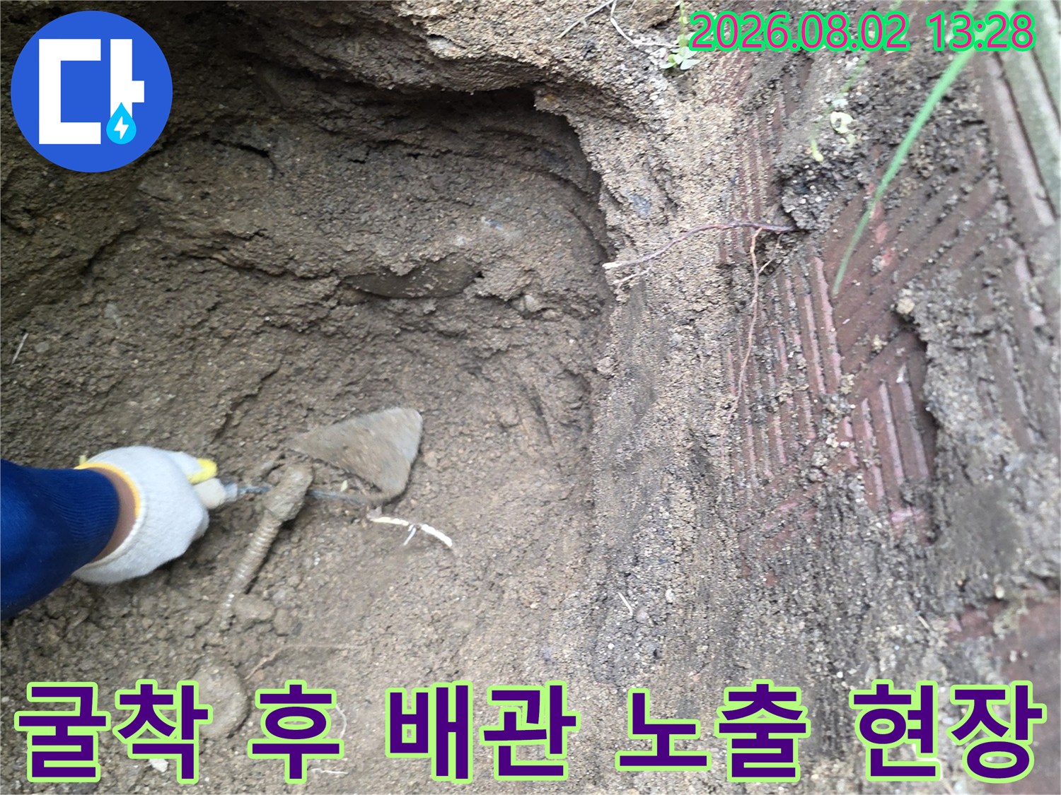 흙을 파내고 드러난 매립 배관과 작업자의 손이 겹쳐진 모습