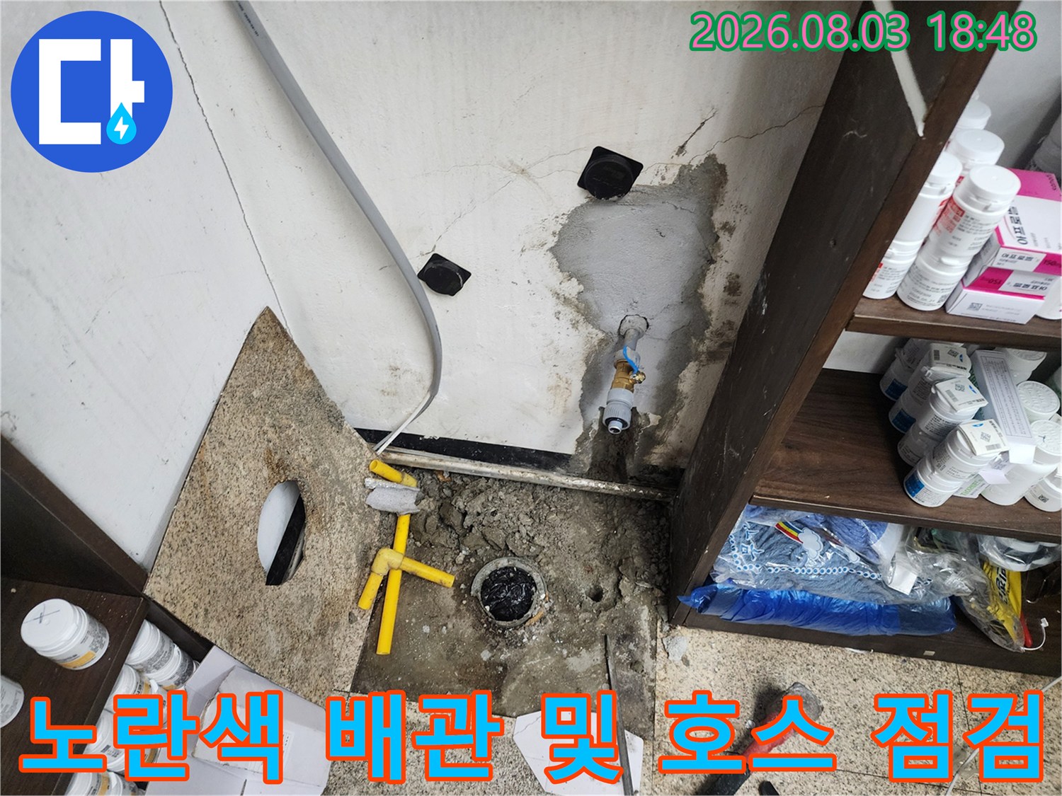 물에 젖은 싱크대 하부 공간에서 노란색 배관과 연결부를 확인하는 사진