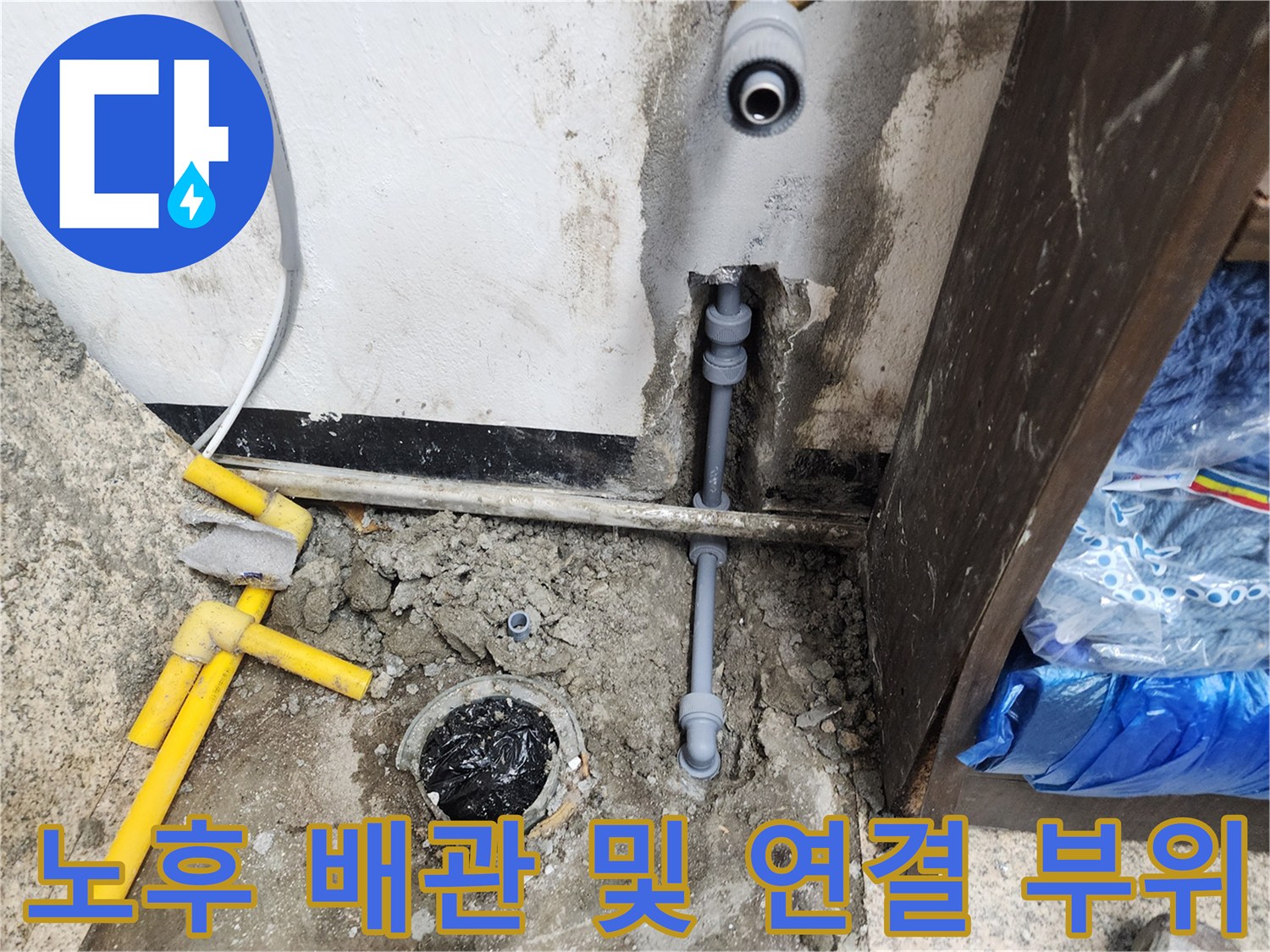 싱크대 하단 벽면 틈새로 노출된 회색 배관과 파손된 마감 상태를 촬영한 사진입니다.