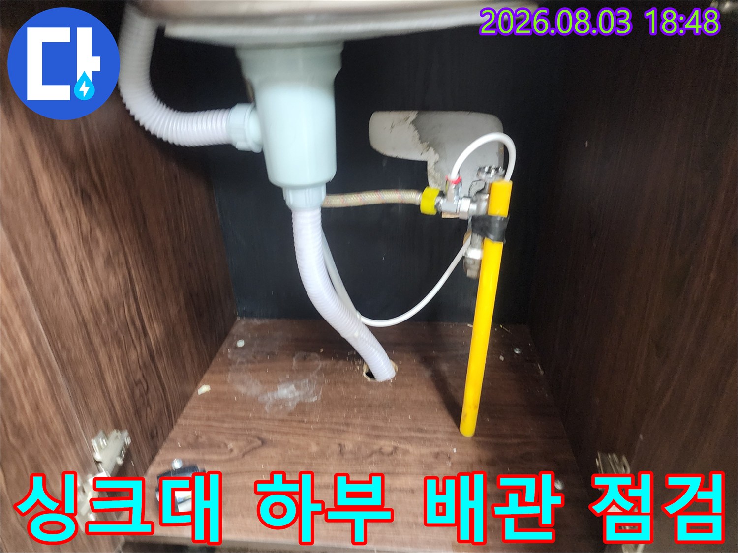 싱크대 하부에 노출된 흰색과 노란색 배관 연결 부위 점검 장면