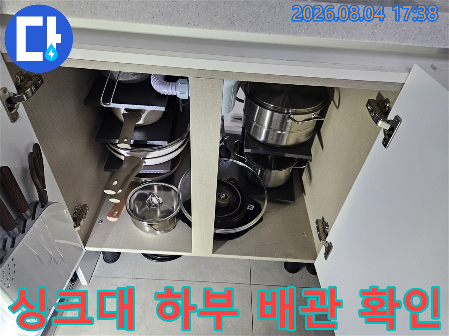 주방 싱크대 아래 수납공간 내부에 위치한 온수 및 급수 배관 상태를 점검하는 모습