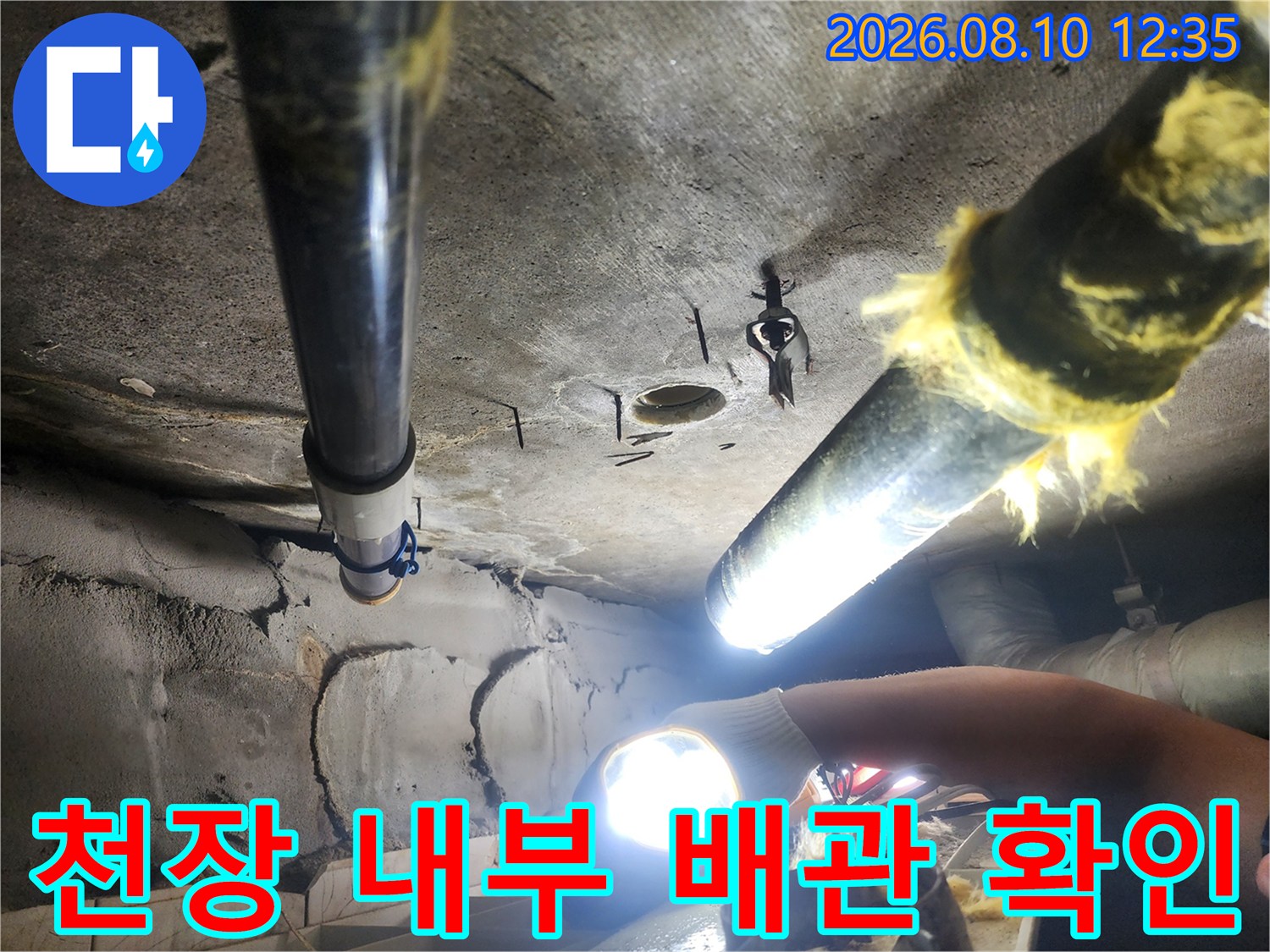 손전등을 사용하여 어두운 천장 속 배관 연결부를 조사하는 모습