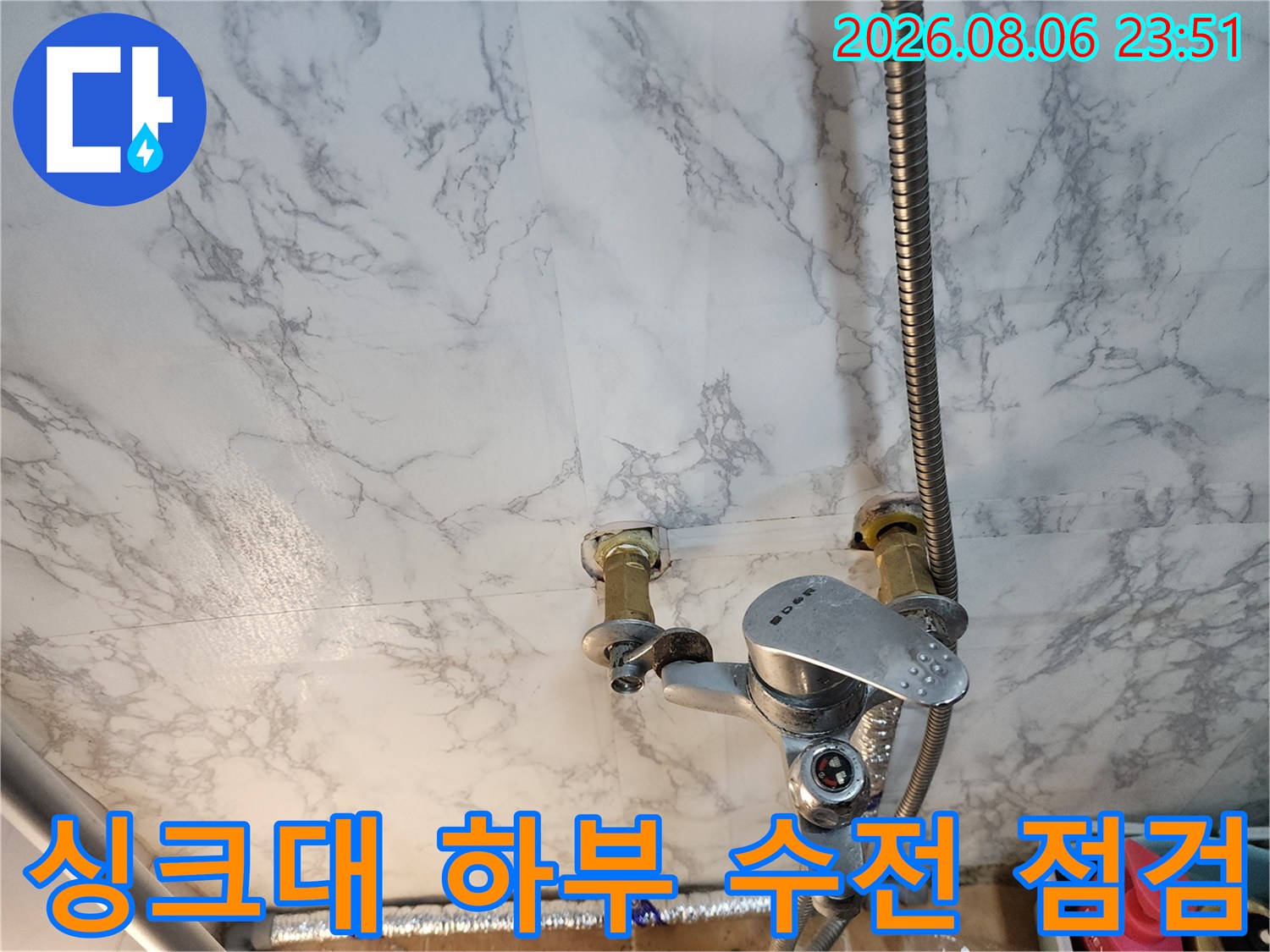 벽면 타일과 연결된 수도 수전의 은색 호스 및 부속품 상세 이미지입니다.