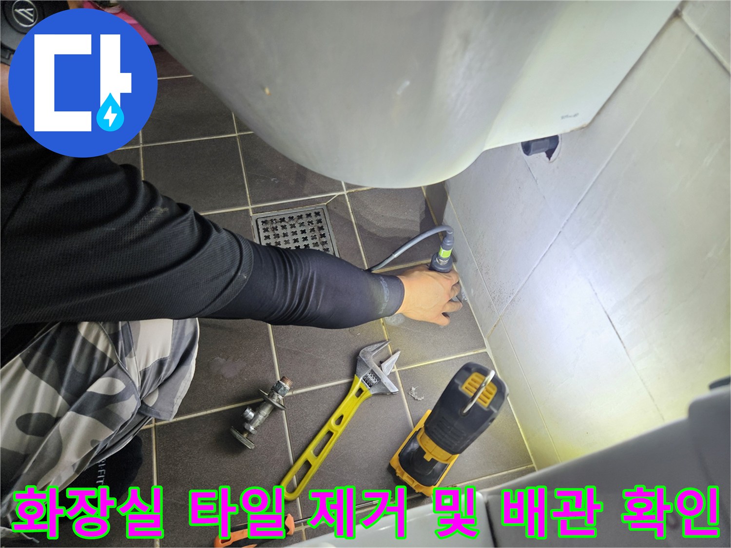 드릴을 사용하여 벽면 타일을 제거하며 내부 배관의 누수 지점을 찾는 작업 모습입니다.