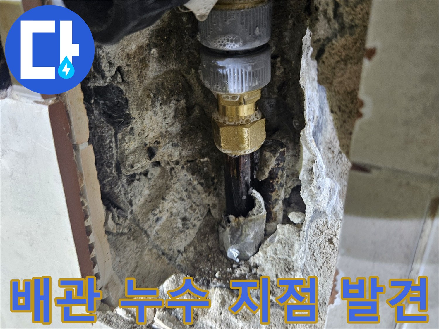 타일 제거 후 드러난 금속 수도 배관의 부식된 연결부와 젖은 벽면
