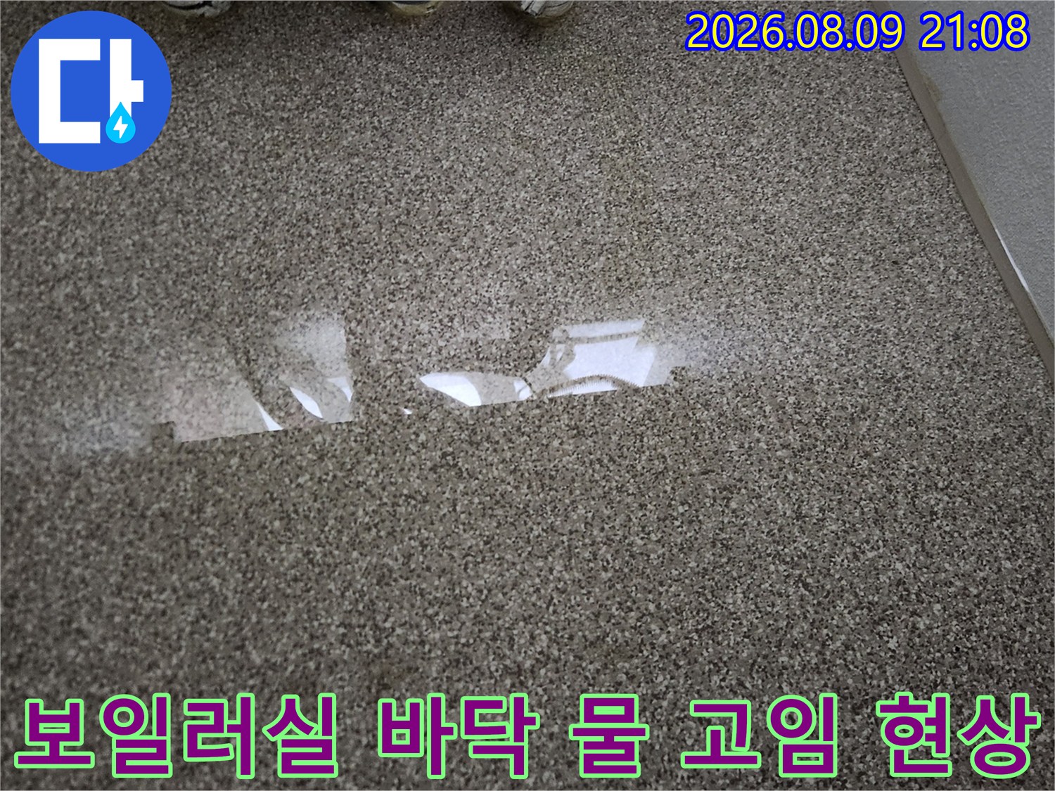 보일러실 내부의 회색 테라조 타일 바닥에 누수로 인해 물이 흥건하게 고여 있는 모습