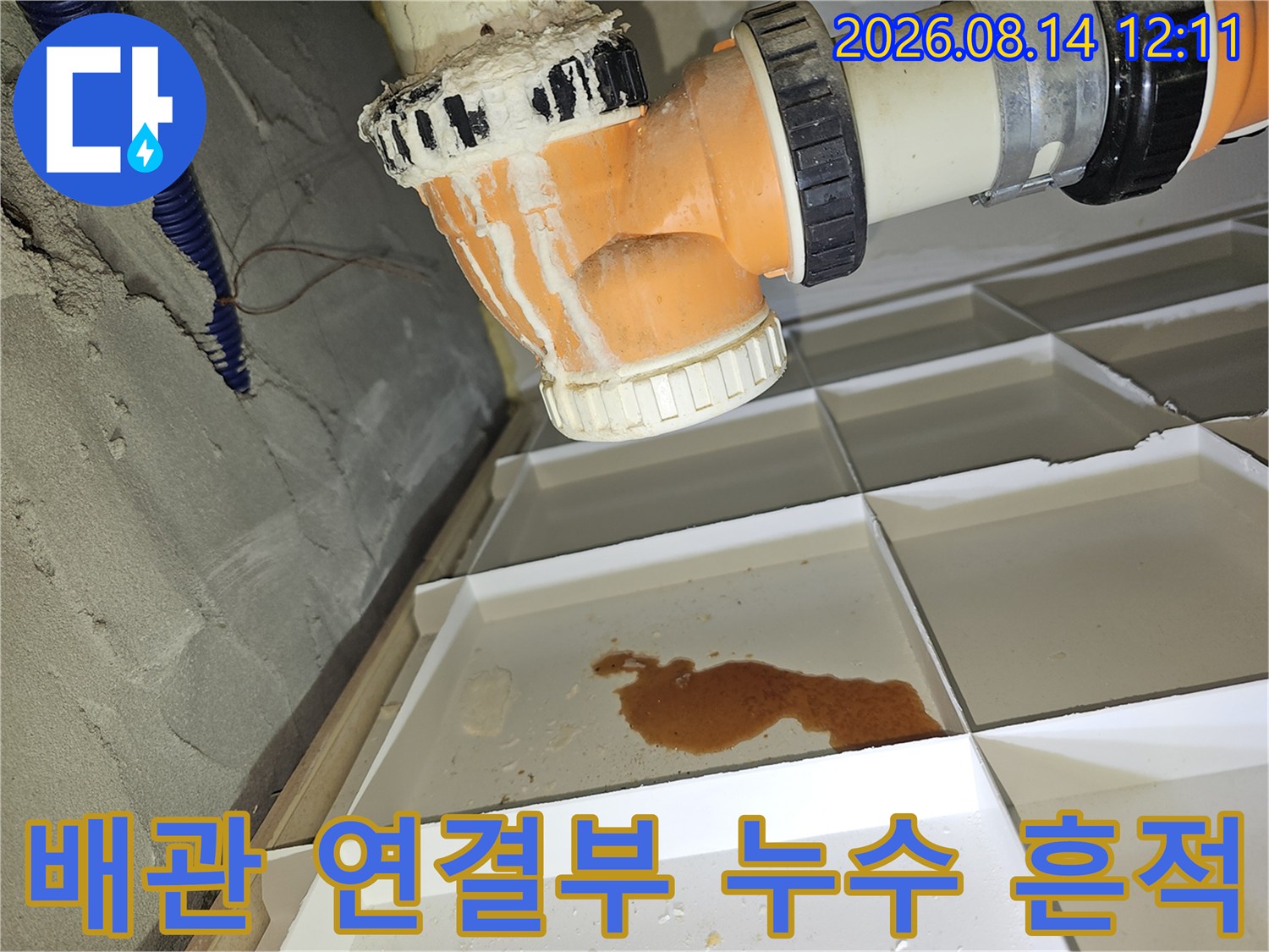 오렌지색 배관 하단부의 갈색 누수 얼룩과 물고임 현상