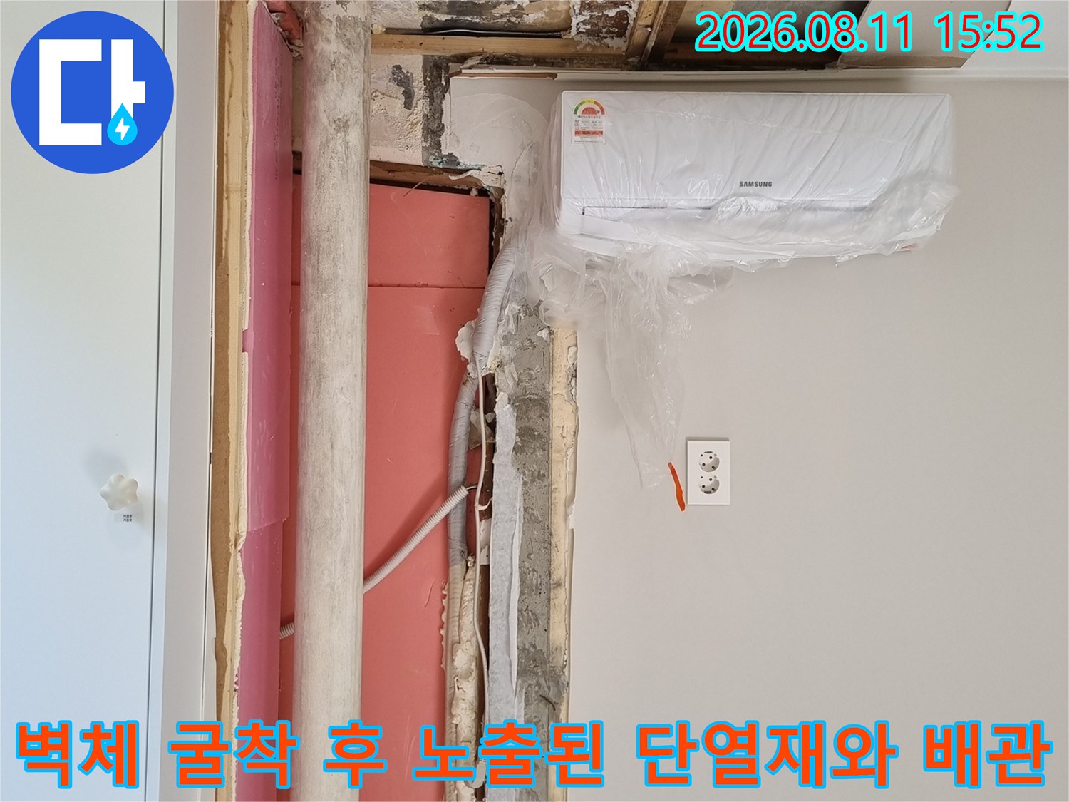 에어컨 아래쪽으로 벽을 파내어 드러난 분홍색 단열재와 흰색 드레인 호스-누수 분석 중