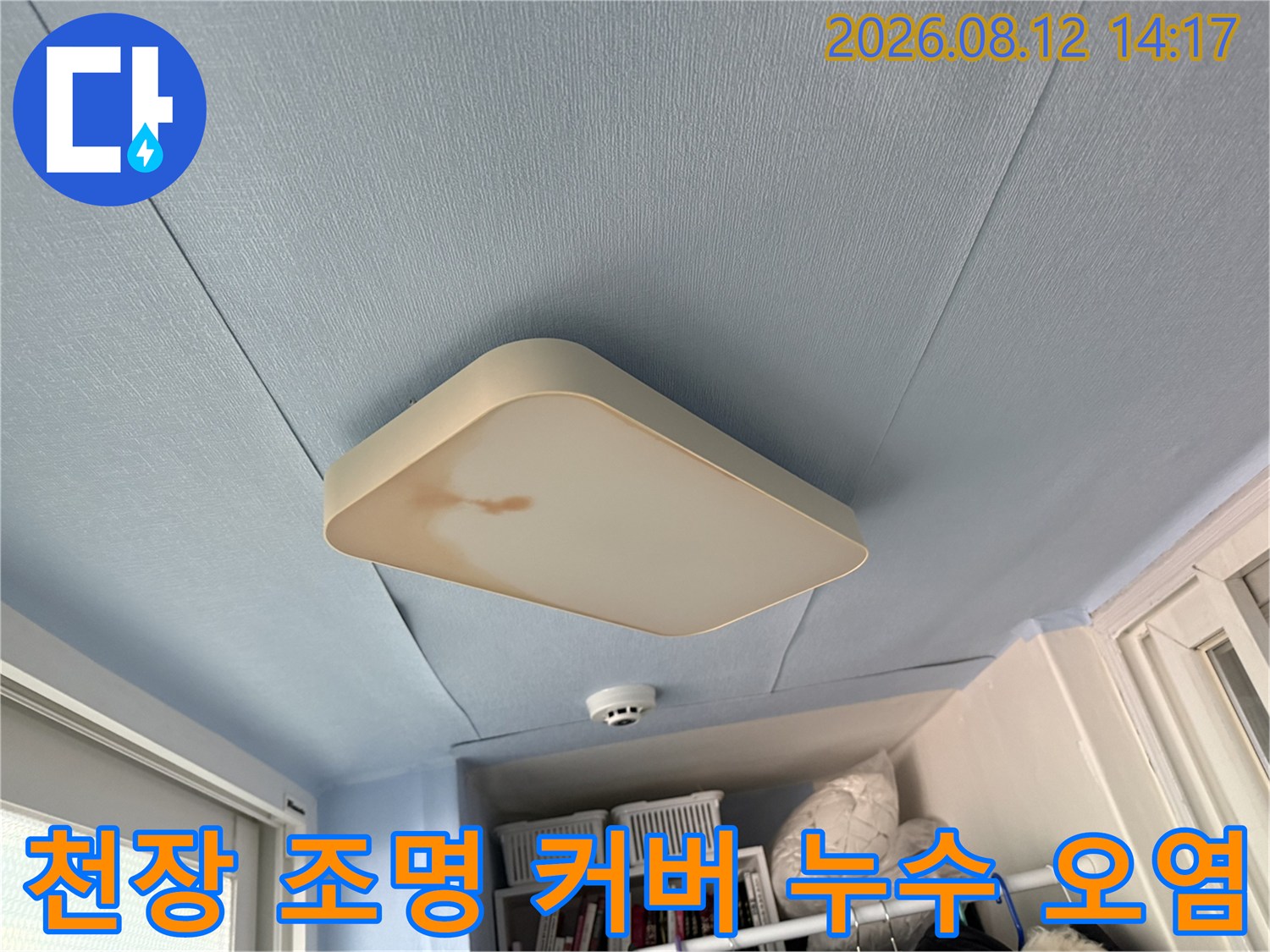 하늘색 베란다 천장에 설치된 흰색 조명 기구 주변에 발생한 갈색 누수 얼룩