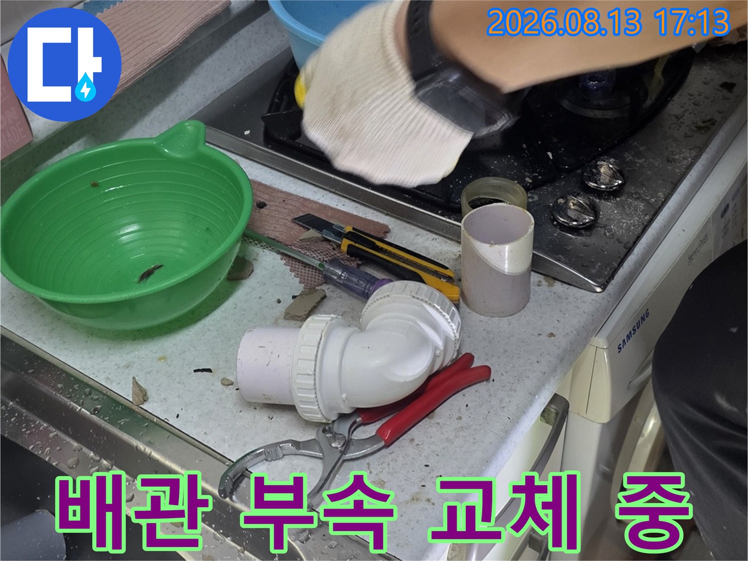 하얀색 배관 연결 부품과 공구들이 놓여 있는 싱크대 하단 작업 모습입니다.