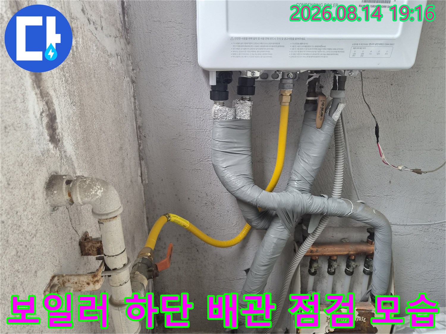 보일러 아래쪽의 회색 테이핑된 배관과 노란색 배관의 연결부를 촬영한 이미지입니다.