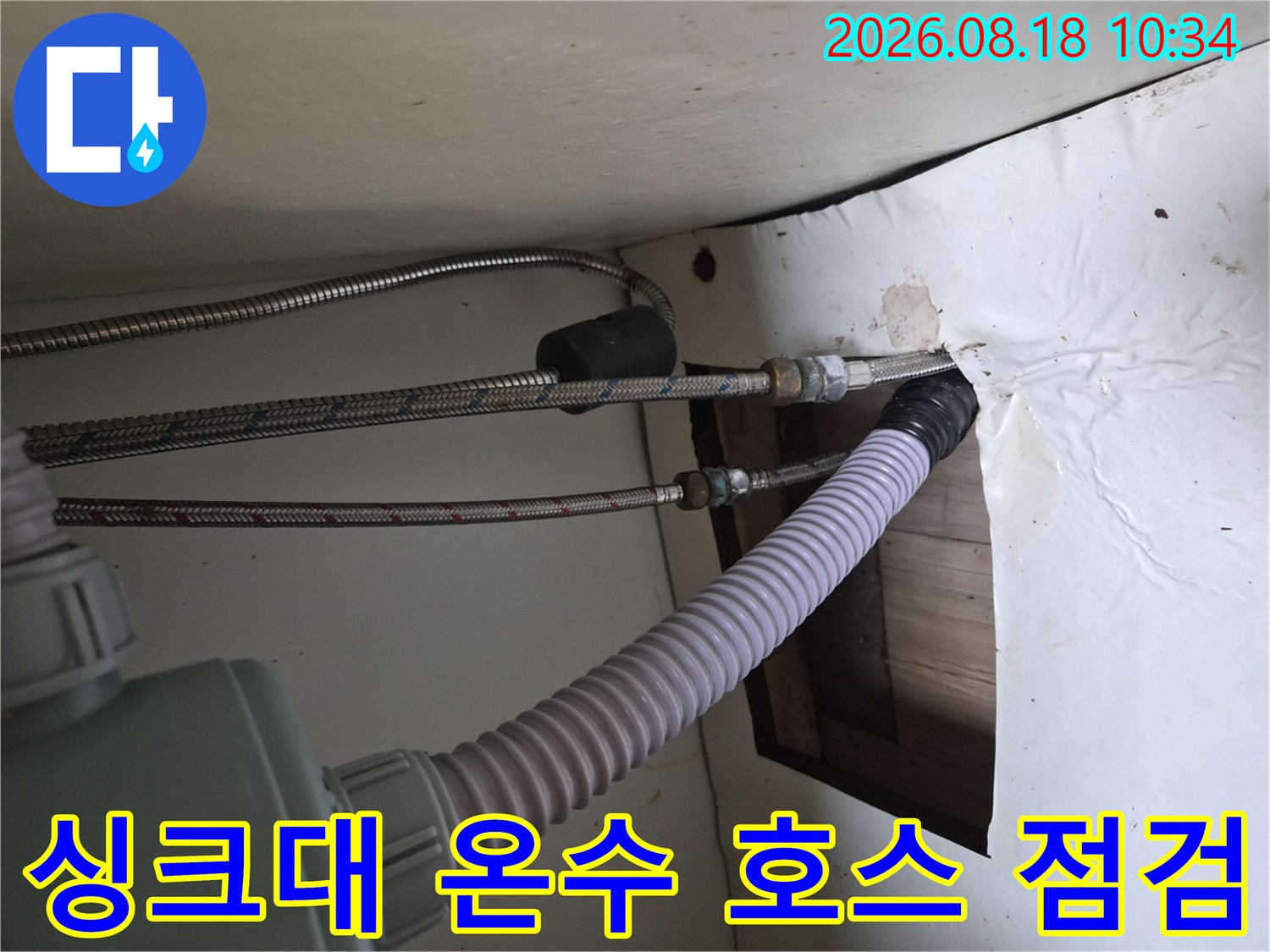 은색 고압 호스와 흰색 주름 배수관이 연결된 싱크대 내부 모습