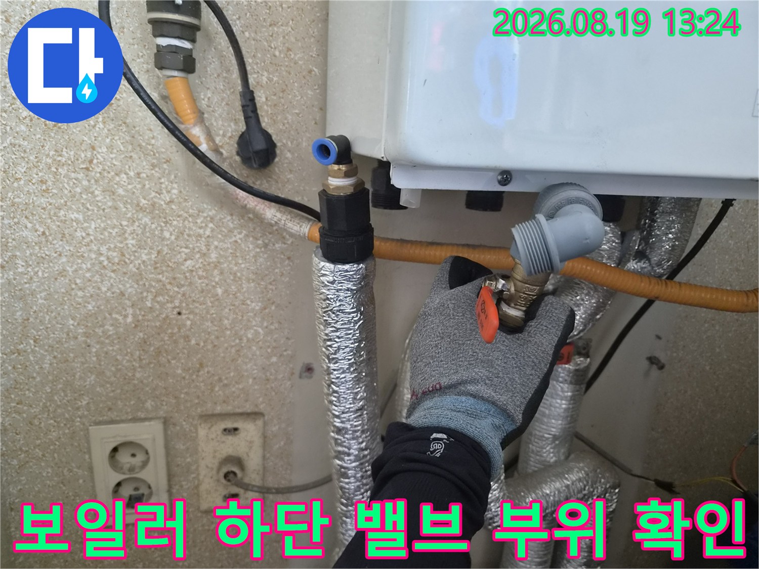 장갑을 낀 작업자가 보일러 아래쪽 배관 밸브를 조작하며 점검하고 있습니다.