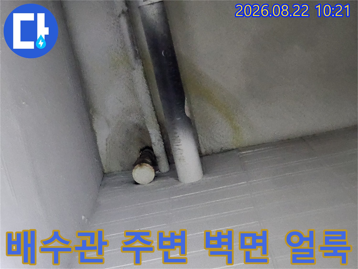 배수관 뒤쪽 벽면에 나타난 습기로 인한 변색과 오염 상태입니다.