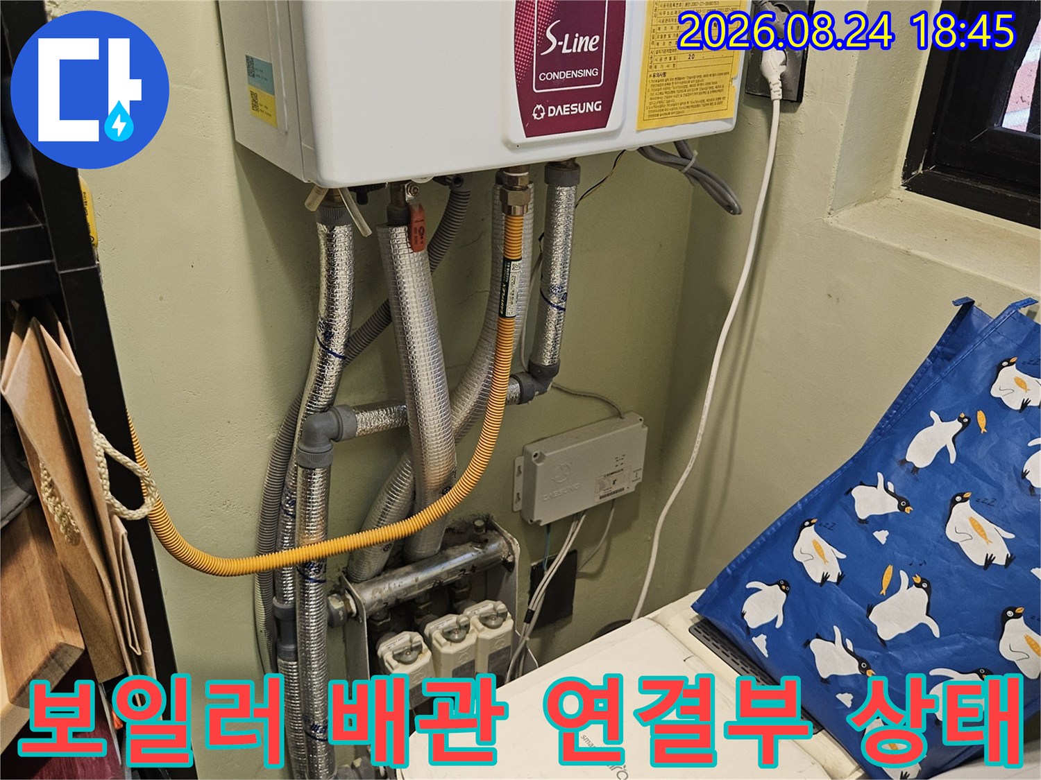 보일러 하단에 연결된 은색 보온재 배관과 노란색 호스 모습입니다.