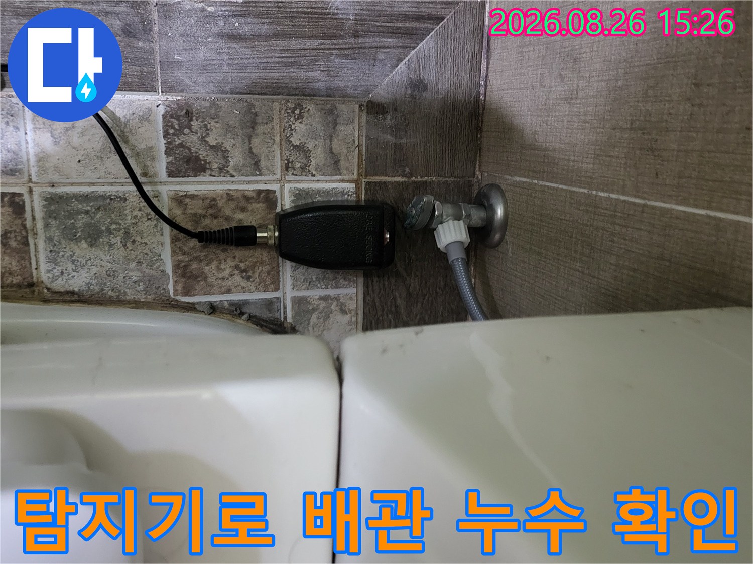 검은색 가스 탐지기 센서를 변기 아래 배관 근처에 대고 누수 여부를 측정하고 있습니다.