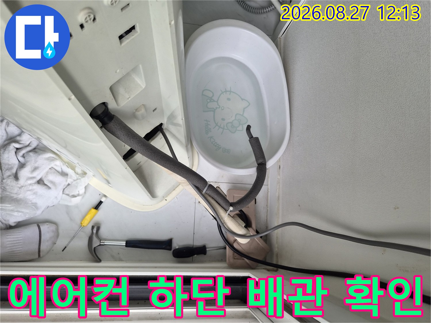 에어컨 아래쪽 배관과 청소용 도구들이 놓인 현장 사진입니다.