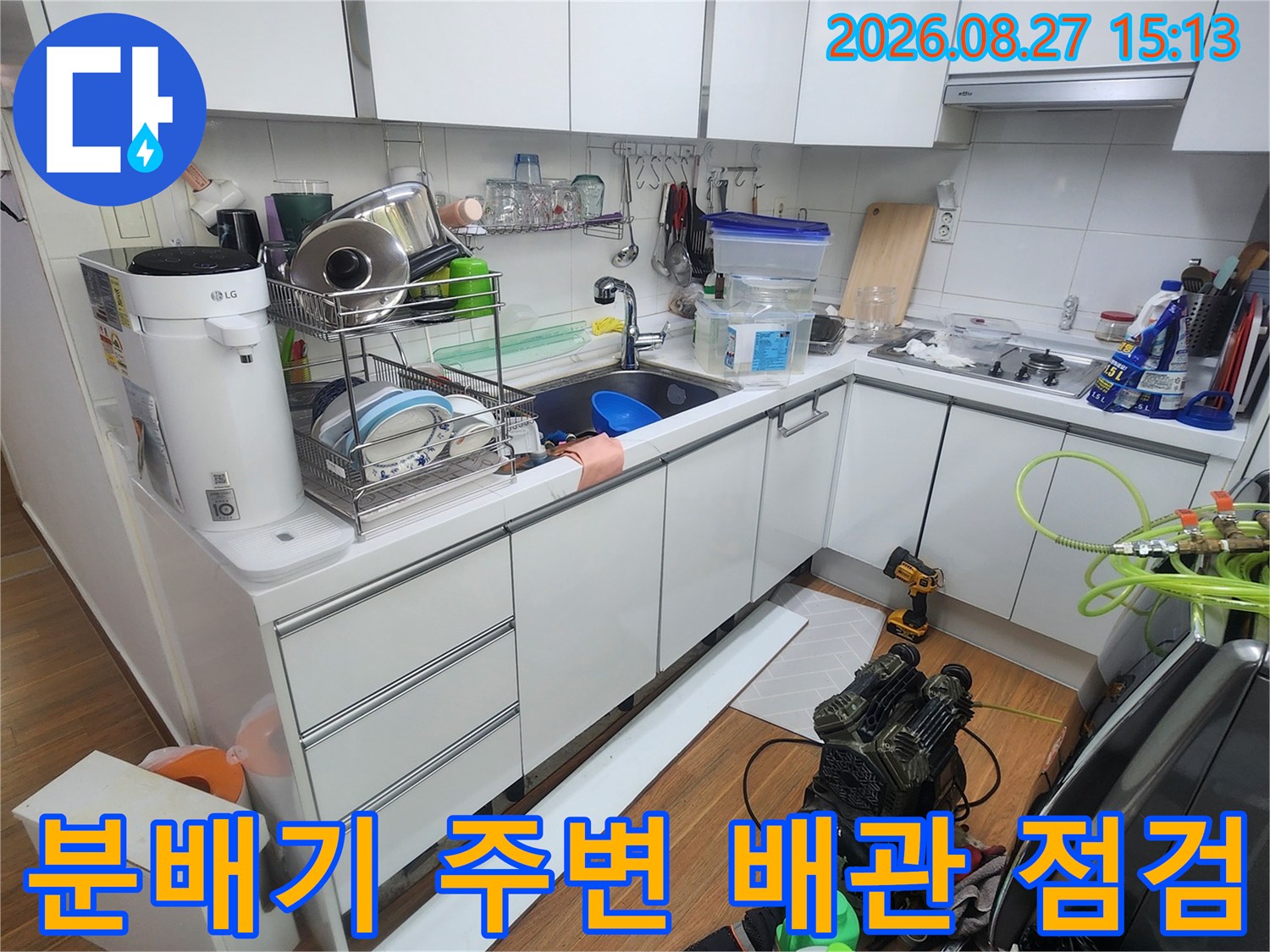 싱크대 하단 공간에 설치된 보일러 분배기와 다양한 배관들의 연결 상태를 보는 사진입니다.